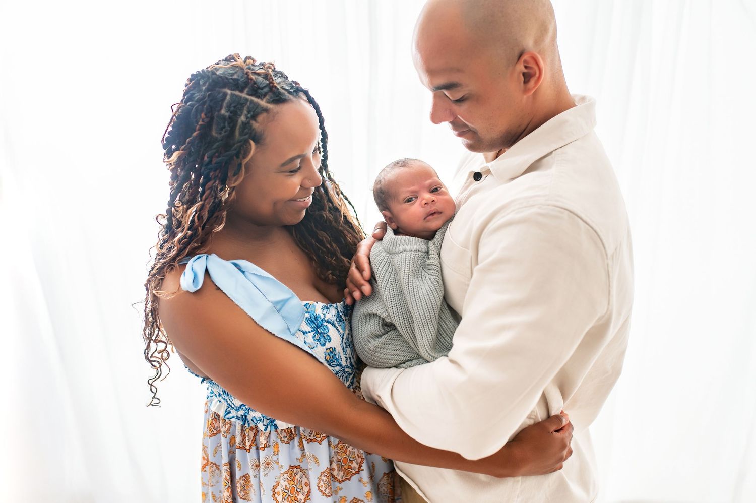 Tender moment between parents holding their newborn baby in bright, airy setting.