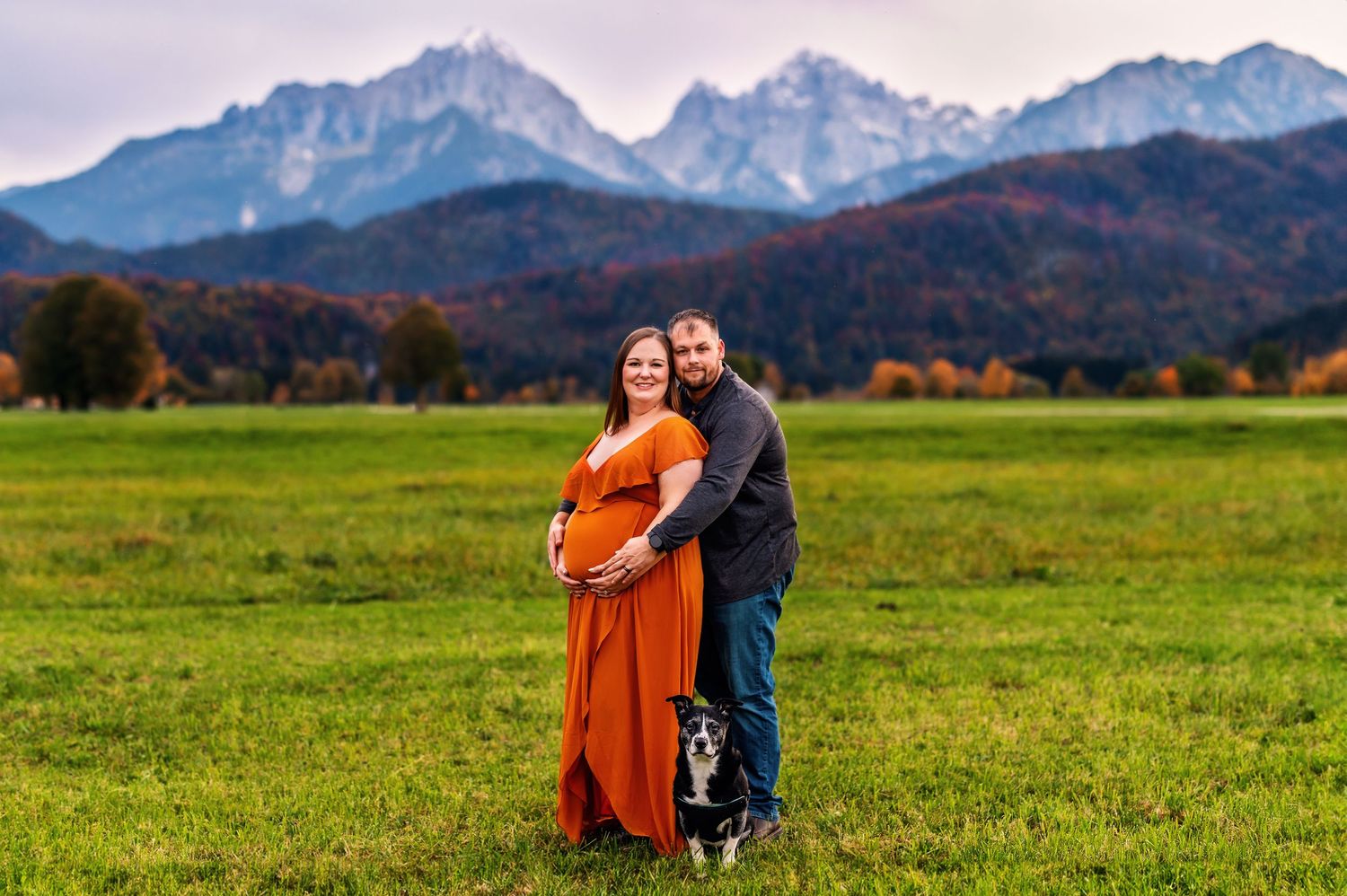 Couple embracing in autumn meadow with mountains and fall foliage backdrop.