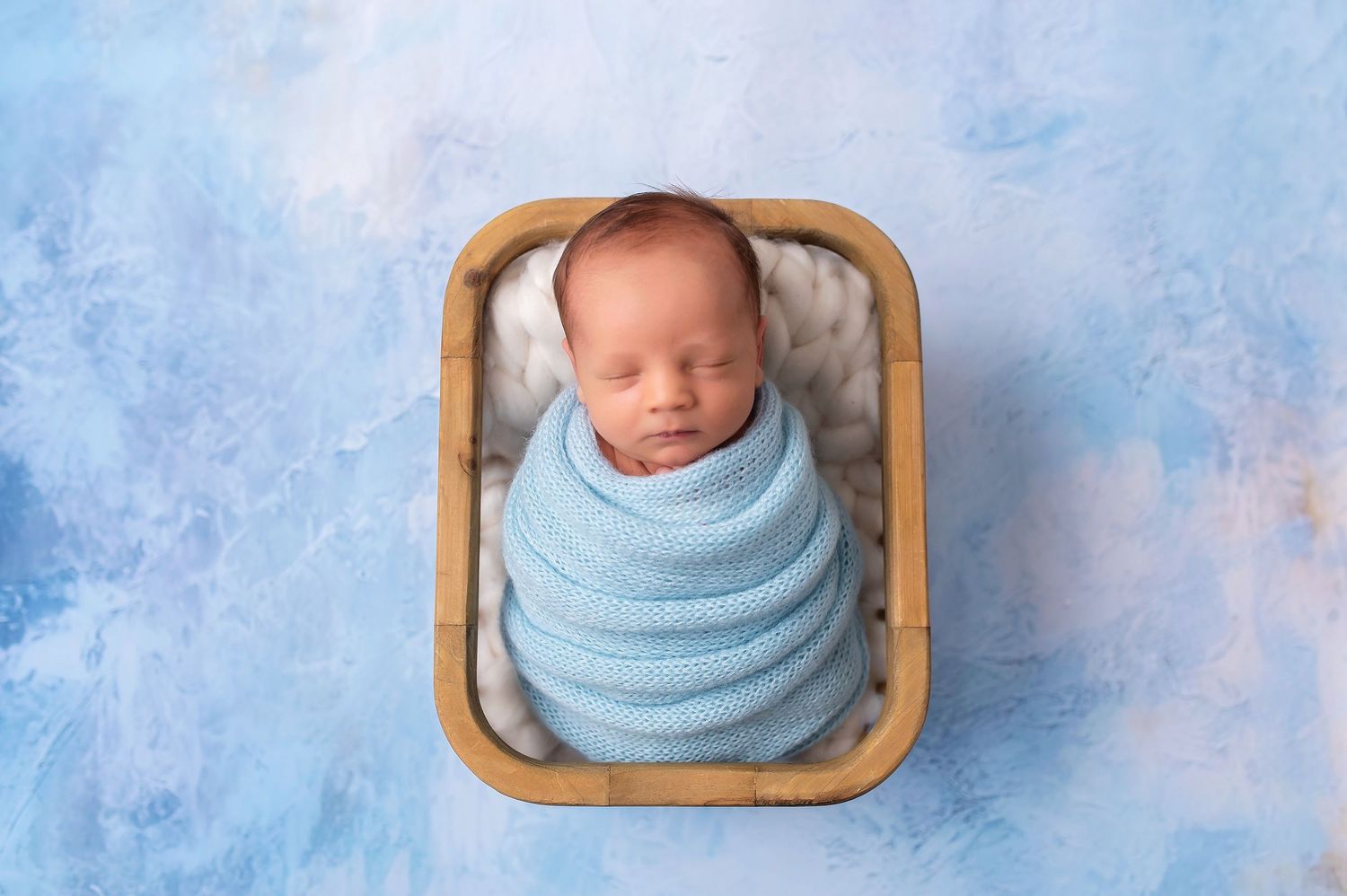 Series of square wooden frames with sleepy newborn posed inside on blue backdrop.