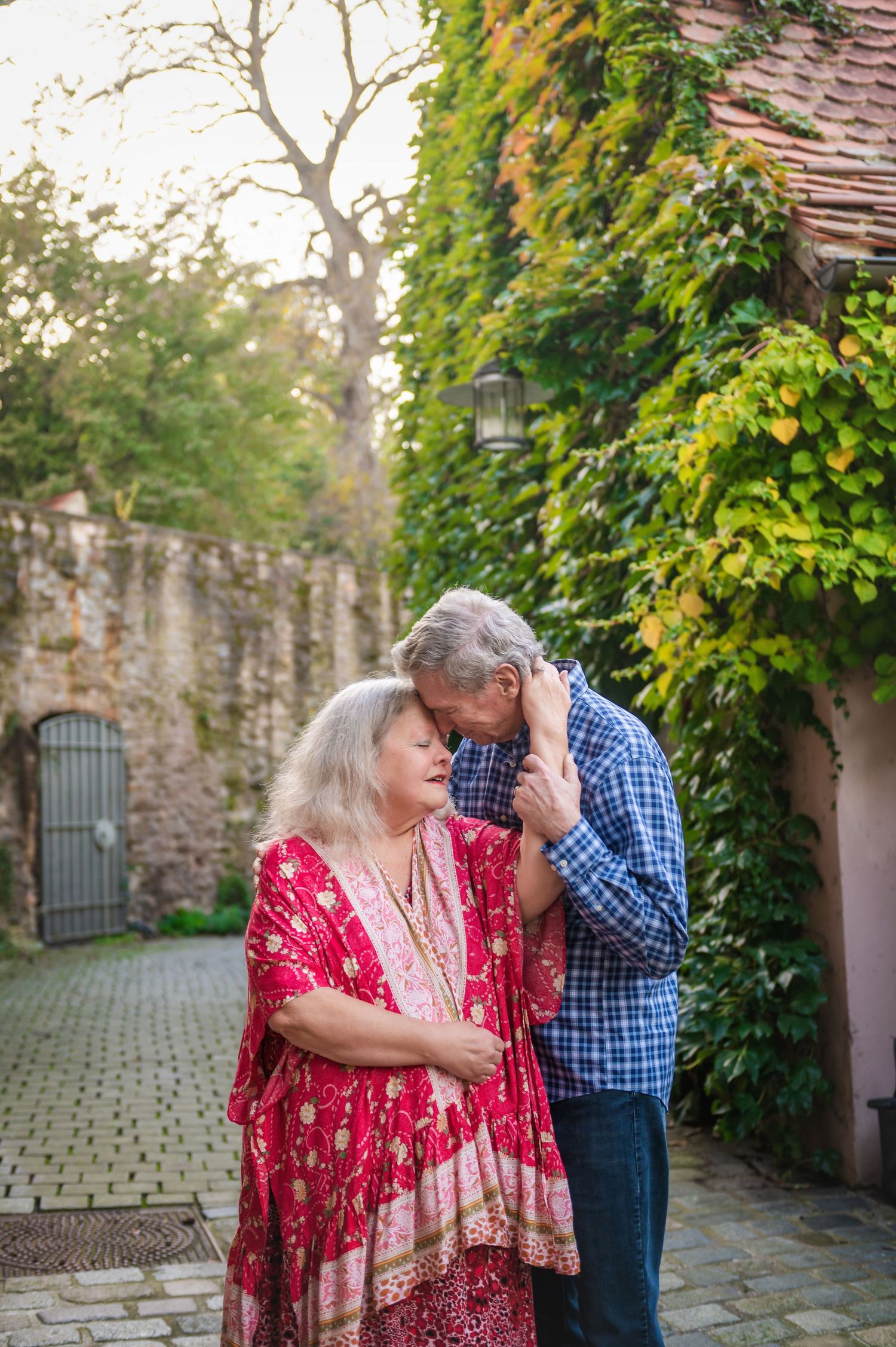 Couple shares intimate moment by ivy-covered stone wall in garden setting.