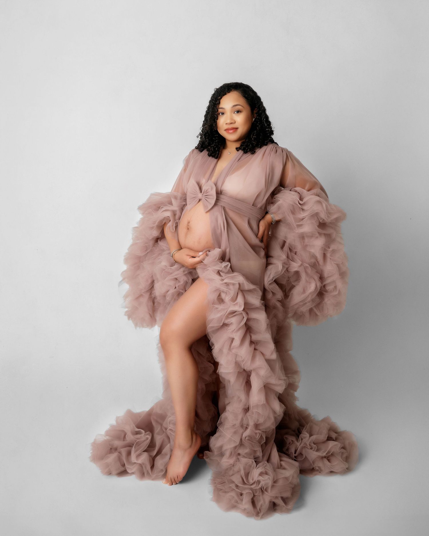 Elegant maternity photo featuring flowing mauve tulle robe against neutral backdrop.