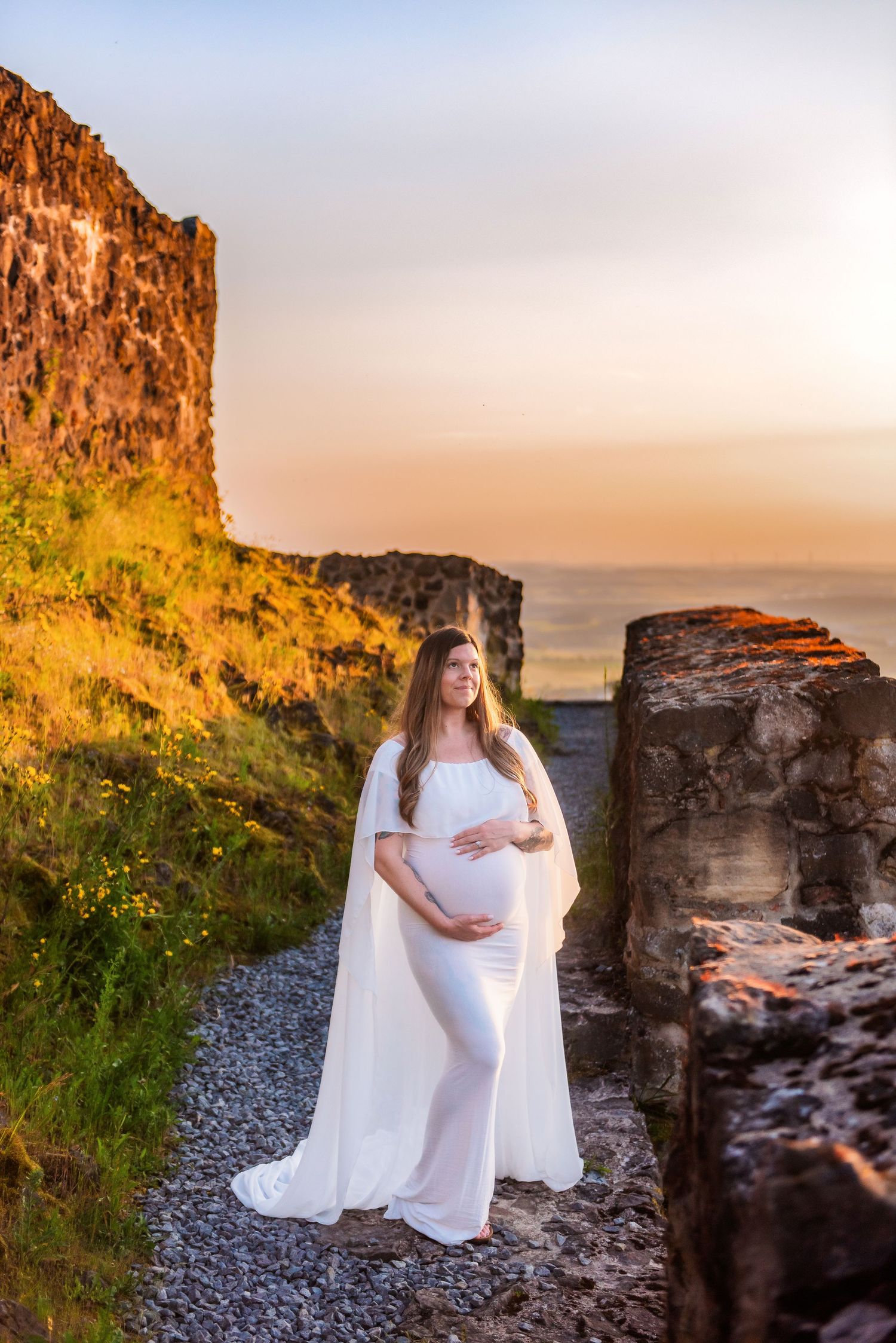 A flowing white maternity dress against dramatic cliffs and countryside at golden hour.