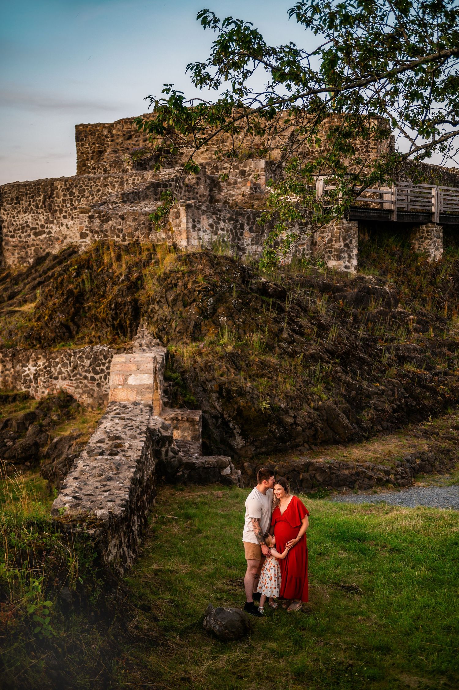 A romantic maternity photo against dramatic castle ruins at sunset.