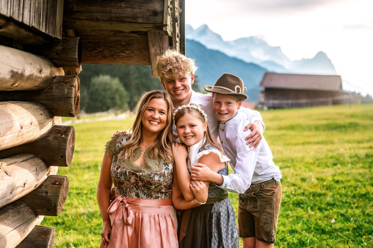 Family enjoying outdoor moments in a scenic mountain meadow with wooden cabin structures in the background.