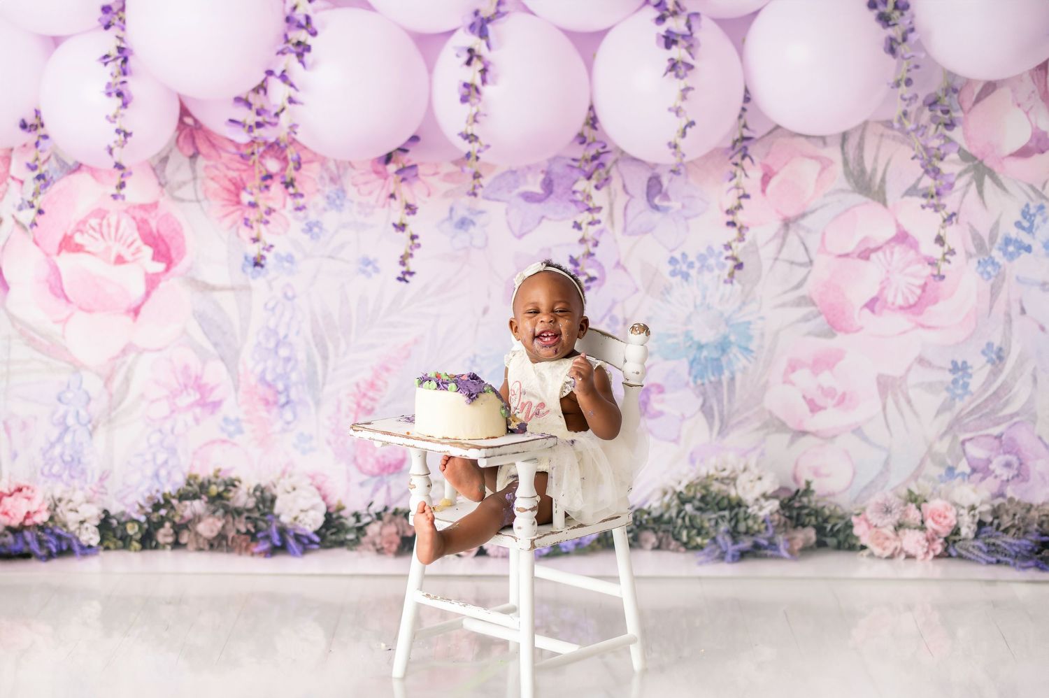 First birthday cake smash photography setup with pink balloons and romantic floral backdrop.