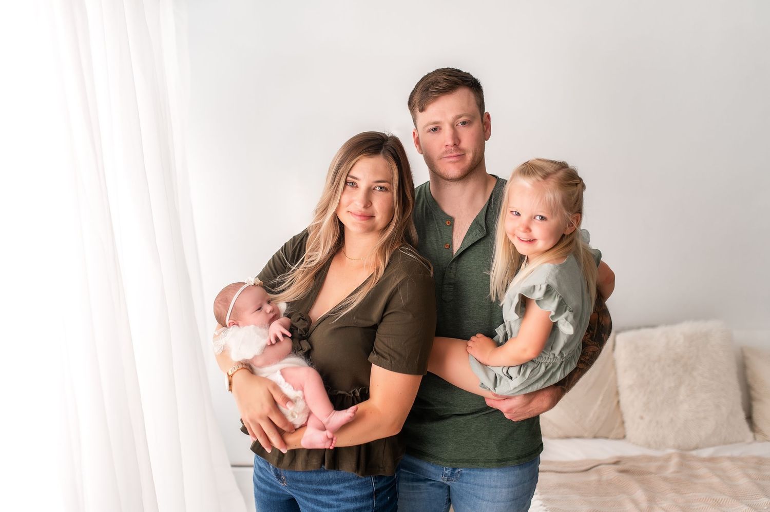 Family studio portrait session with baby in neutral colored outfits on white background.