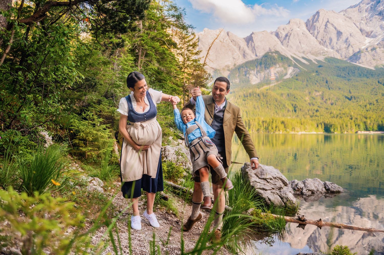 A family in traditional Bavarian clothing poses together by a scenic mountain lake in the Alps.