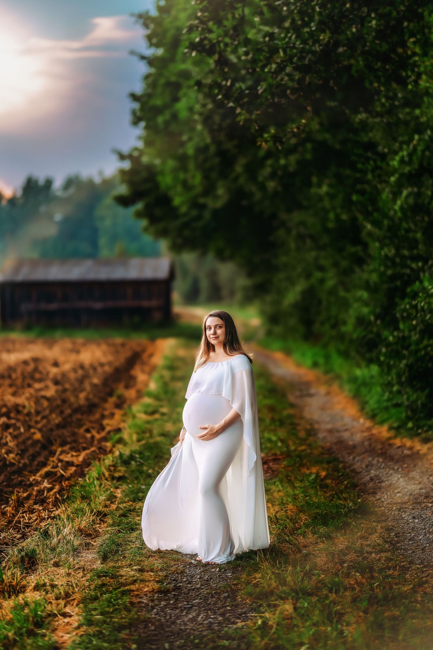 Elegant maternity portrait on a rural dirt path with lush green surroundings.