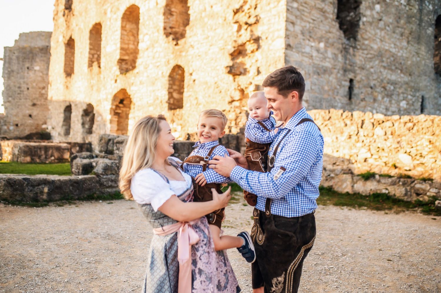 A family poses together in front of ancient stone castle ruins with arched windows.