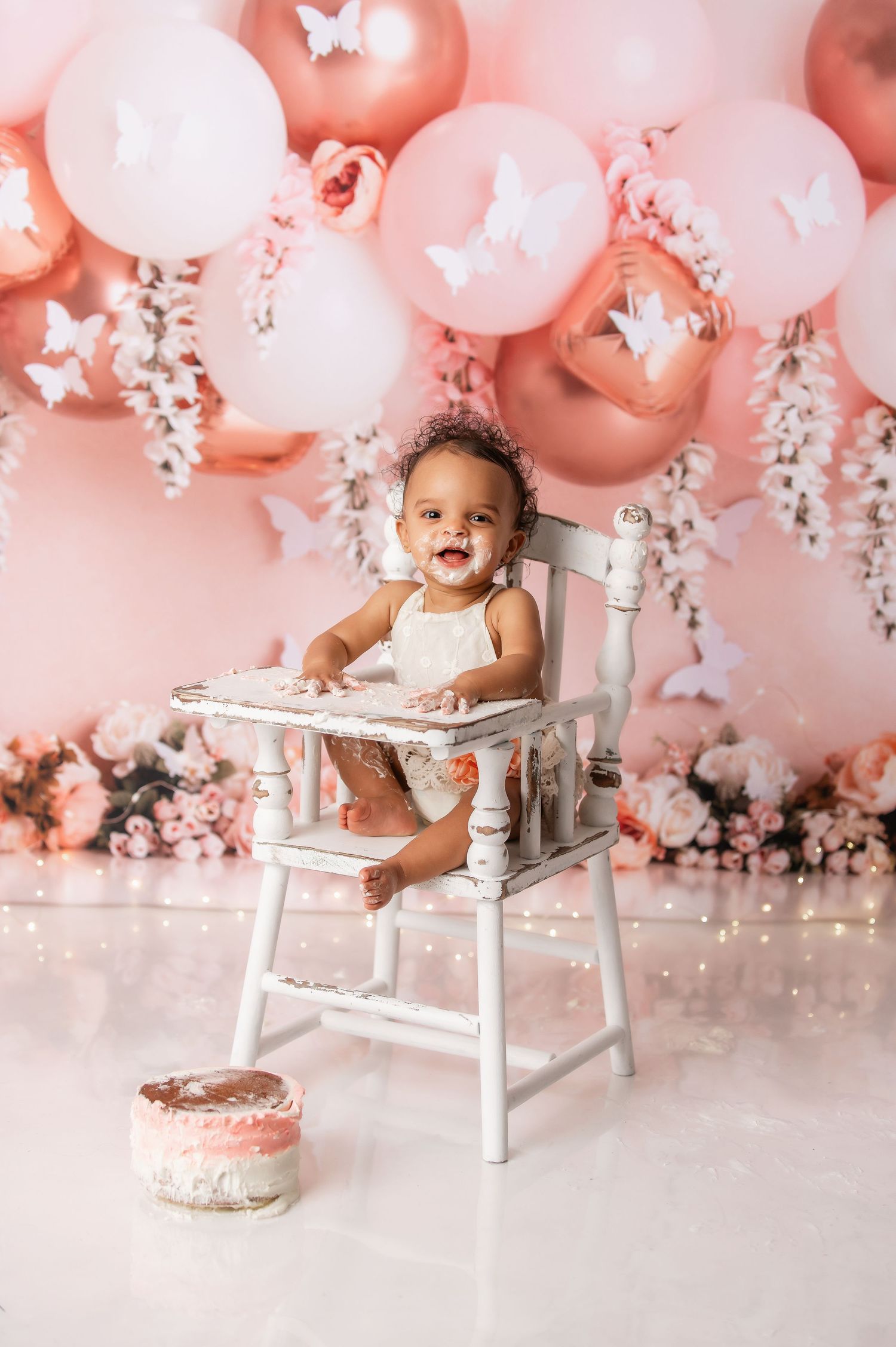 Pink and white balloon backdrop with a white high chair for baby photography session.