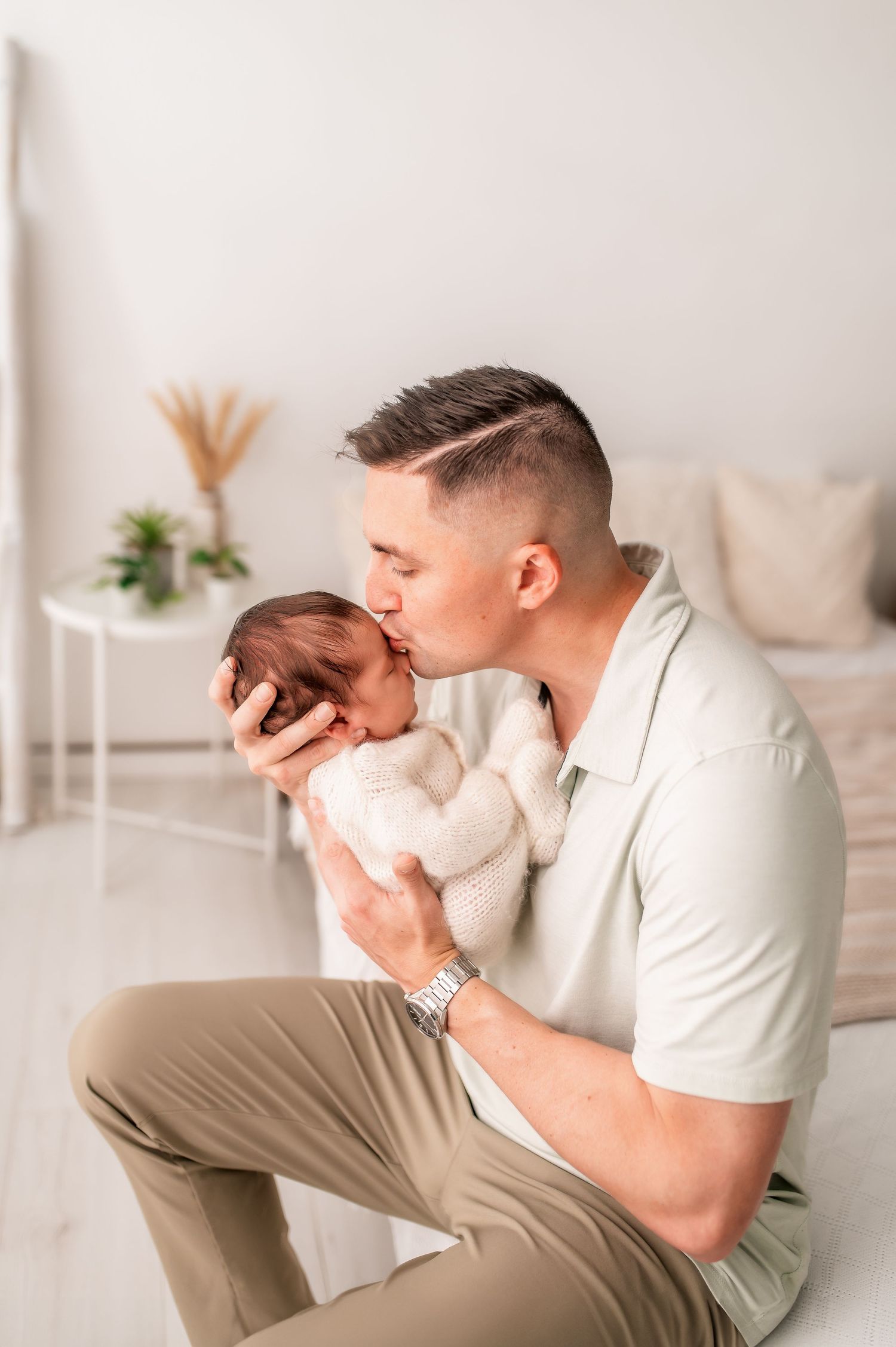 Father bonding with newborn in white modern bedroom setting.