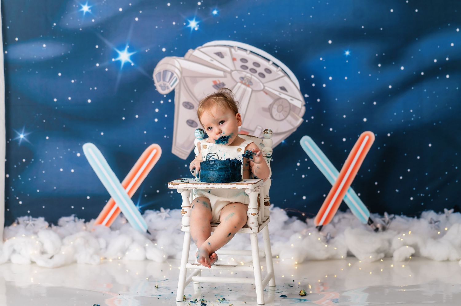 Baby seated in high chair with Star Wars Millennium Falcon backdrop and crossed lightsabers.