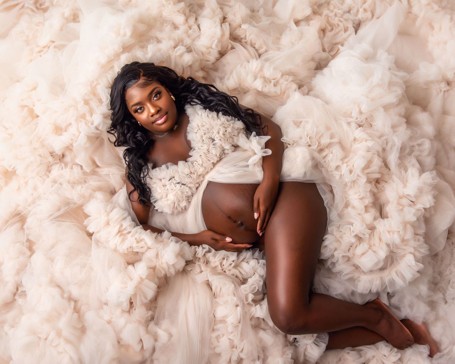 Dreamy maternity portrait with soft cream tulle fabric and romantic styling.