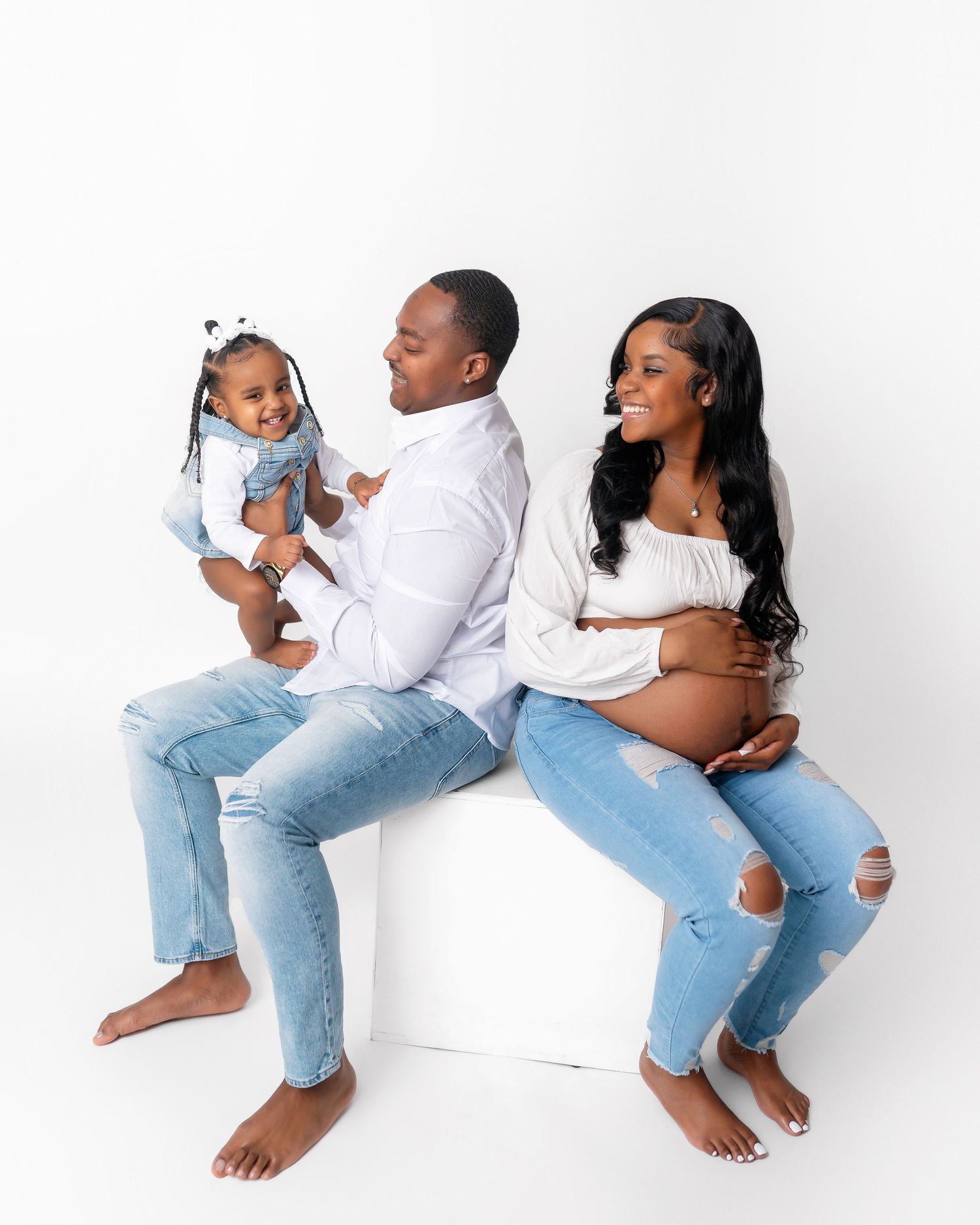 Relaxed family maternity session with parents and toddler in matching casual outfits.