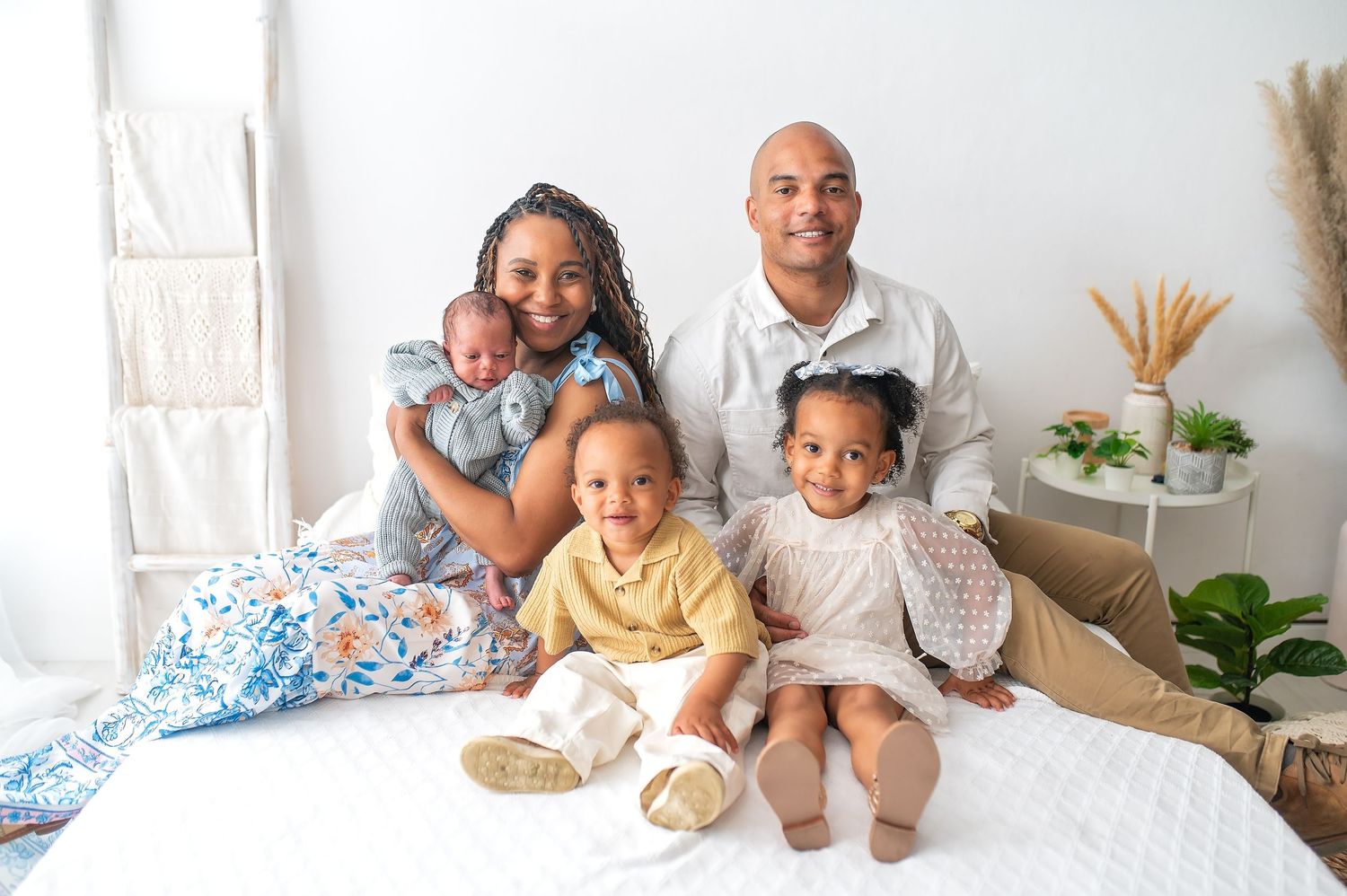 Happy family sitting together on white bed with decorative plants in background.