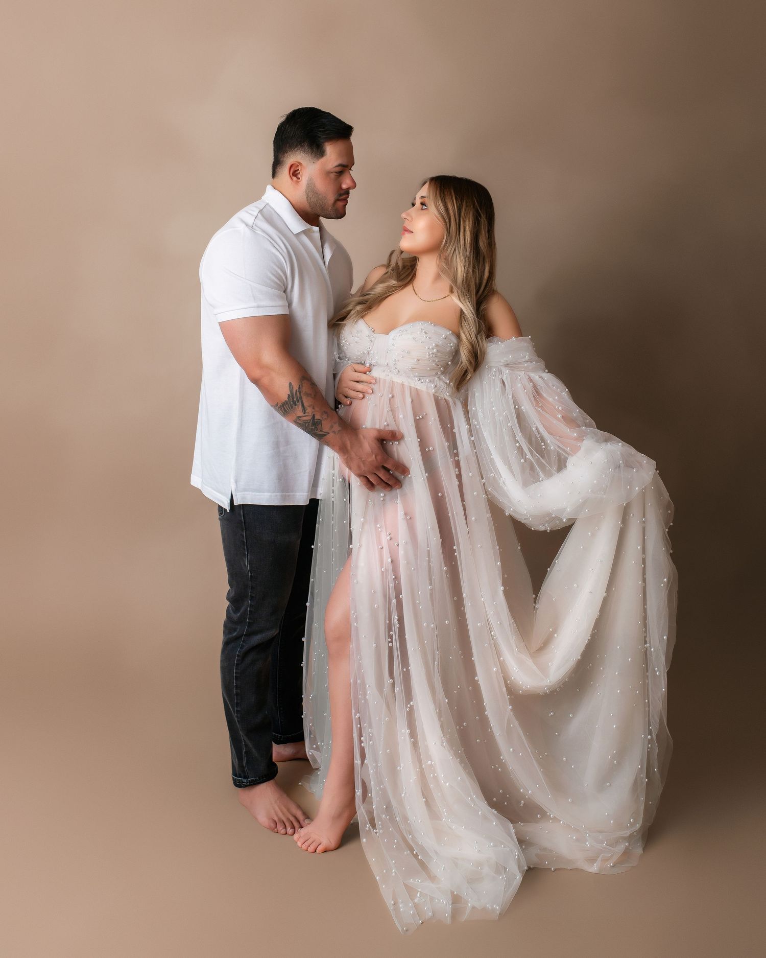 Elegant couple's photoshoot featuring flowy white dress against neutral background.