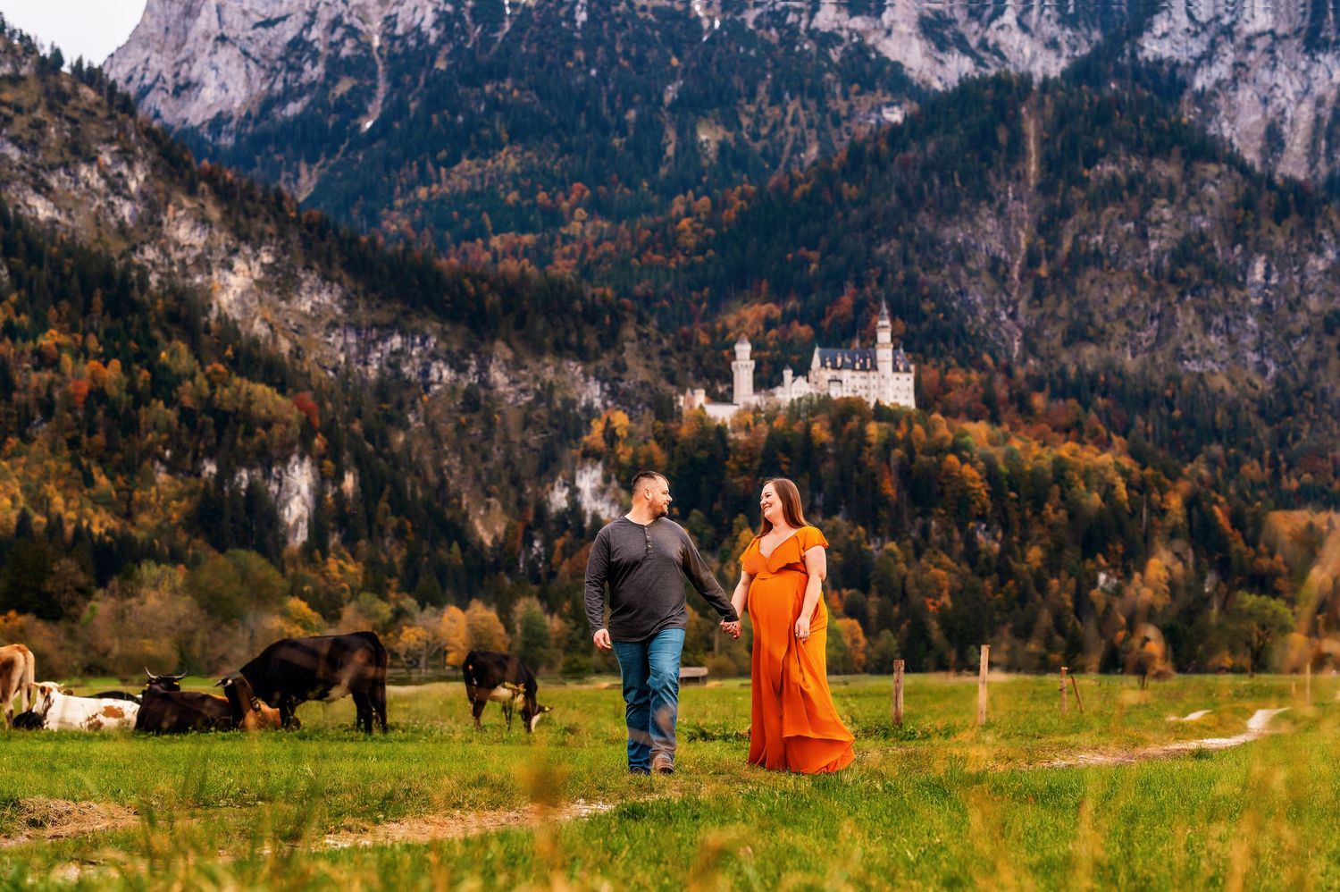 Two people dance in a meadow with historic Neuschwanstein Castle and Bavarian Alps towering in the autumn background.