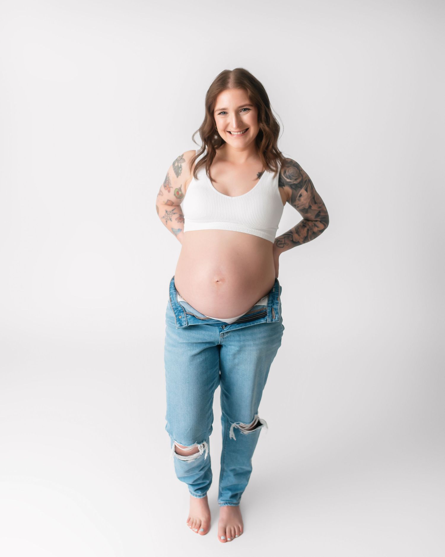 Maternity photoshoot series showing a pregnant woman in distressed jeans and white top against white background.
