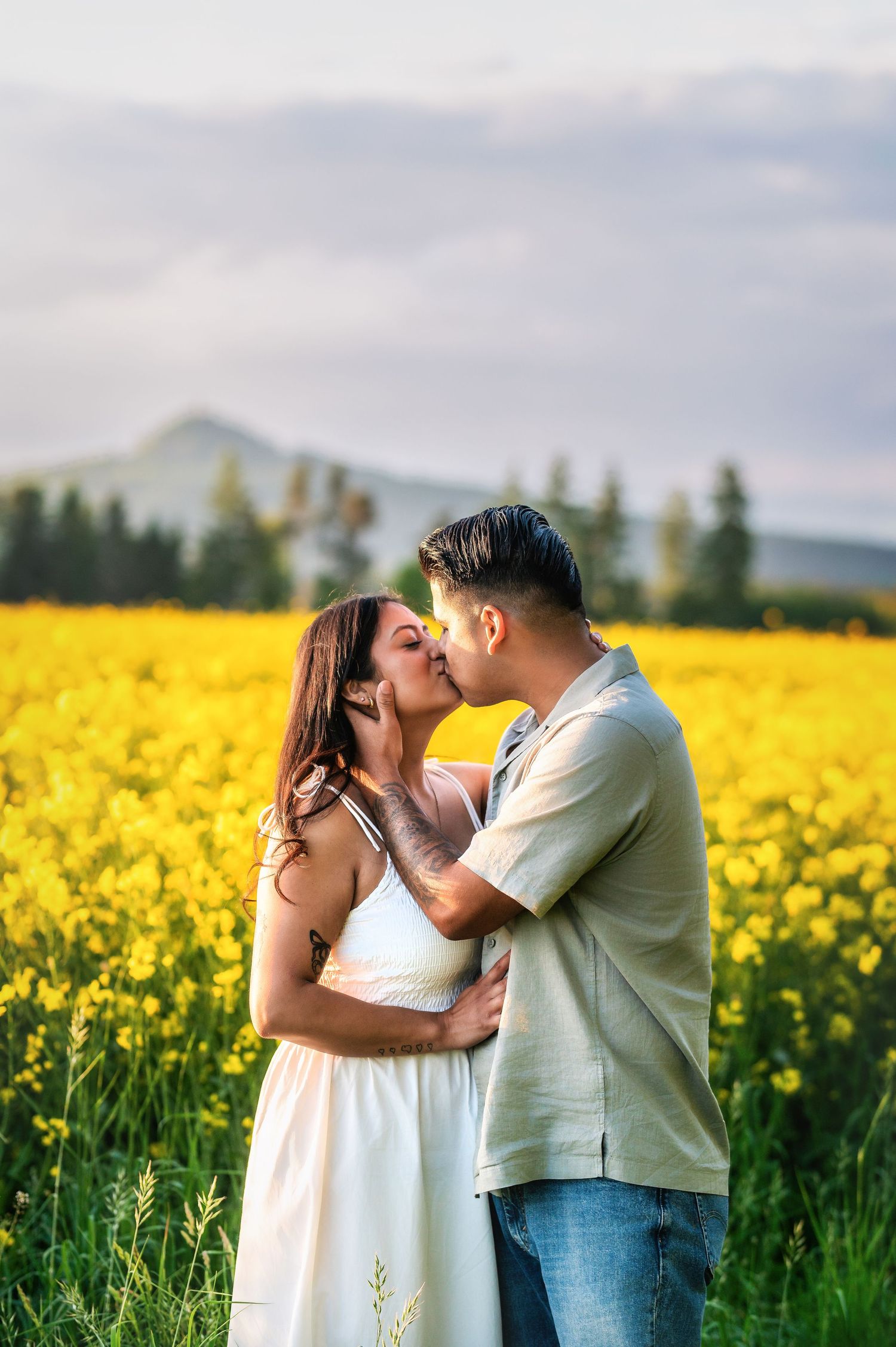 Couple embracing and kissing in a blooming yellow canola field during a spring photoshoot.