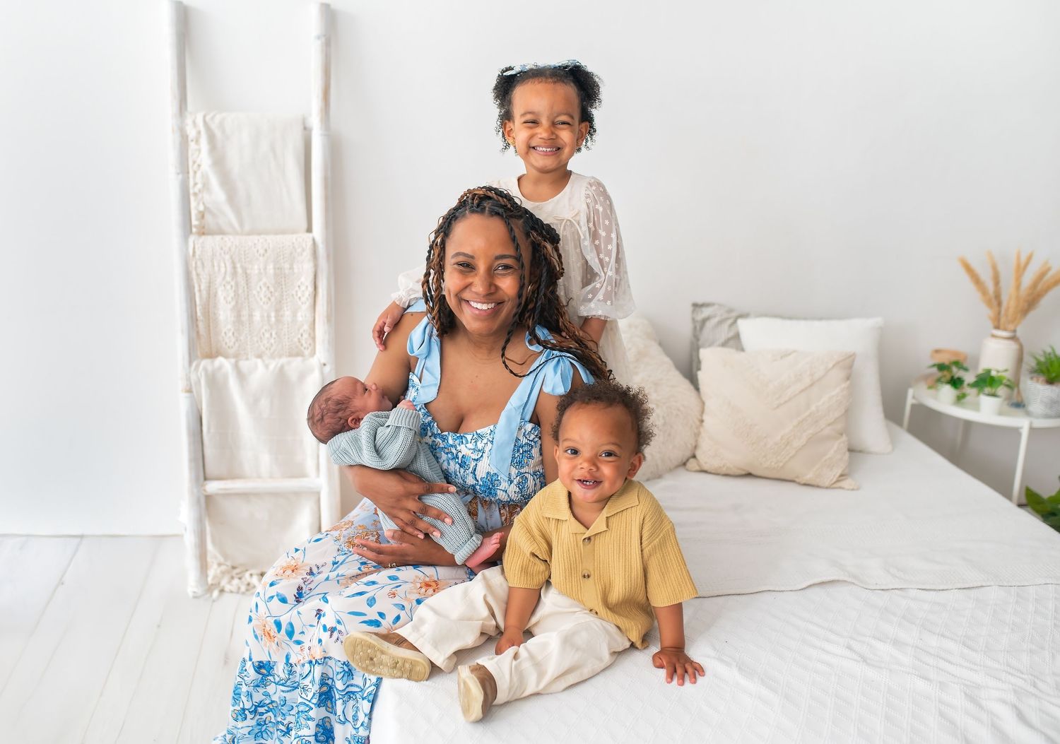 Family portrait on white bed with mother and children in casual setting.