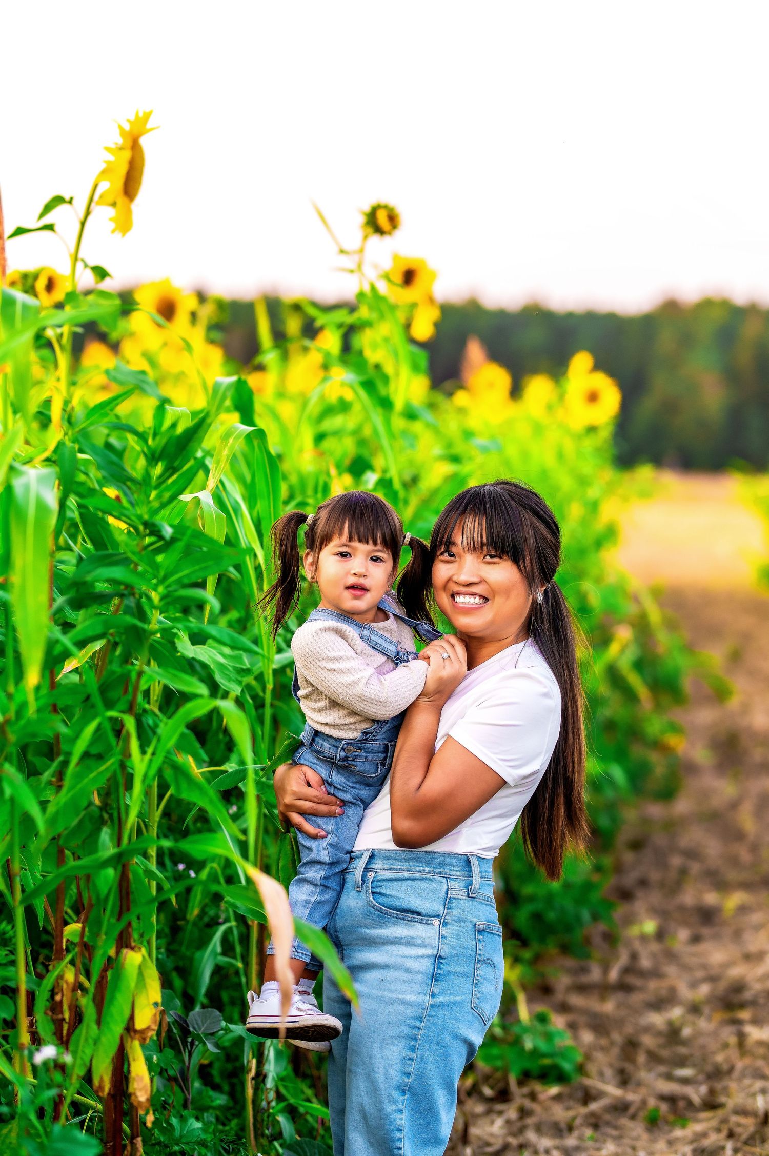 Mother and child share joyful moment together in field of tall sunflowers at golden hour.