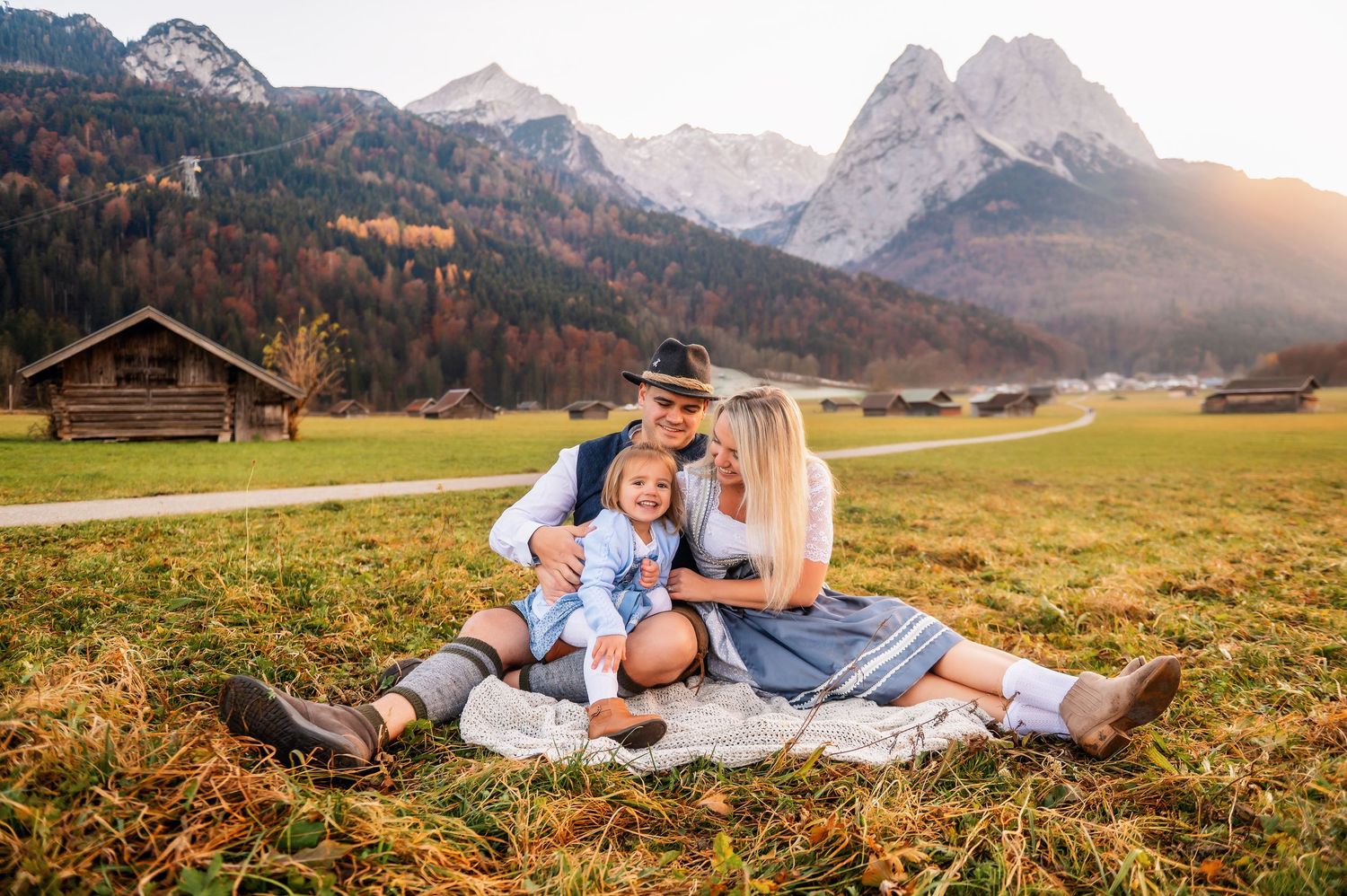 A couple relaxes together on a grassy meadow with majestic snow-capped Alpine mountains in the background at sunset.