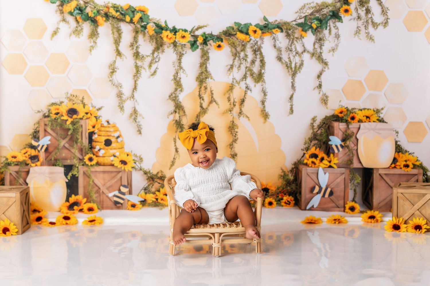 Sunflower themed cake smash photography setup with rustic greenery and yellow floral decorations.