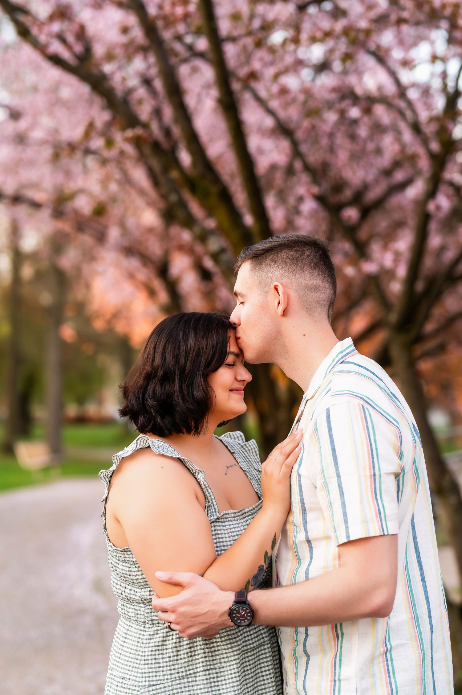 Couple sharing intimate moment under blooming cherry blossom trees during spring photo session.