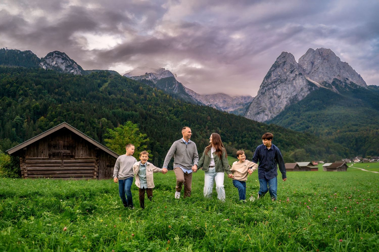 A group walks through a lush green meadow with dramatic mountain peaks and stormy clouds in the Austrian Alps.