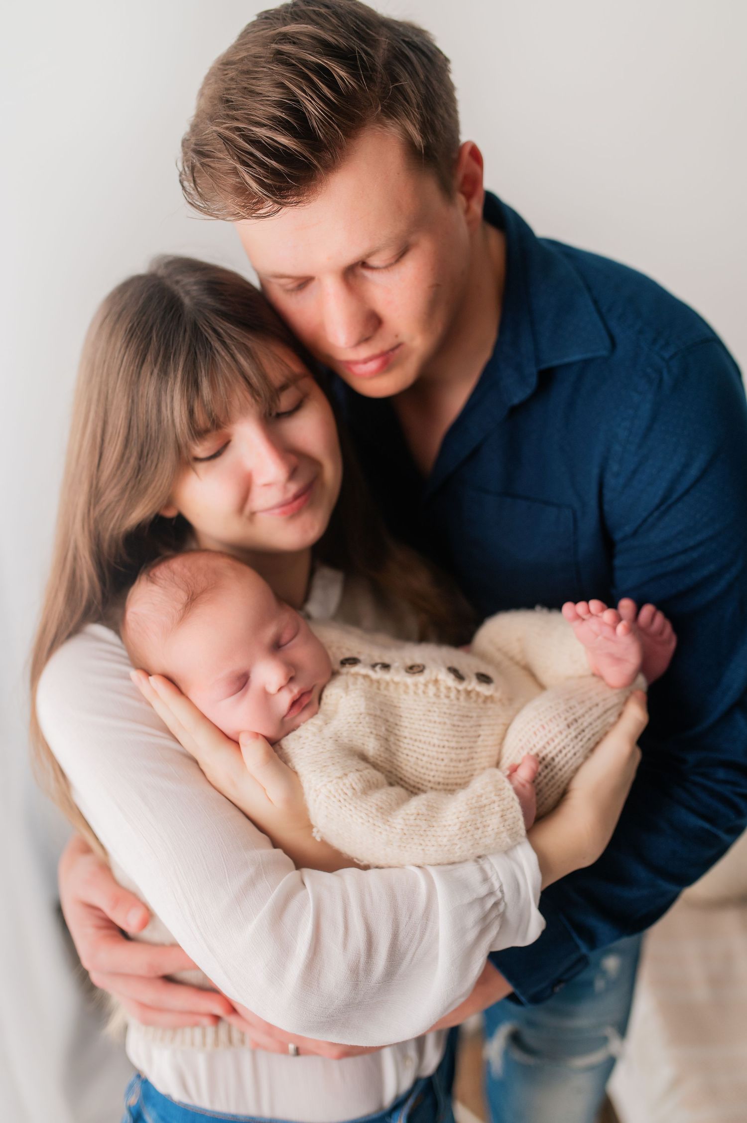 Family portrait series showing parents in white and blue cradling their sleeping newborn.