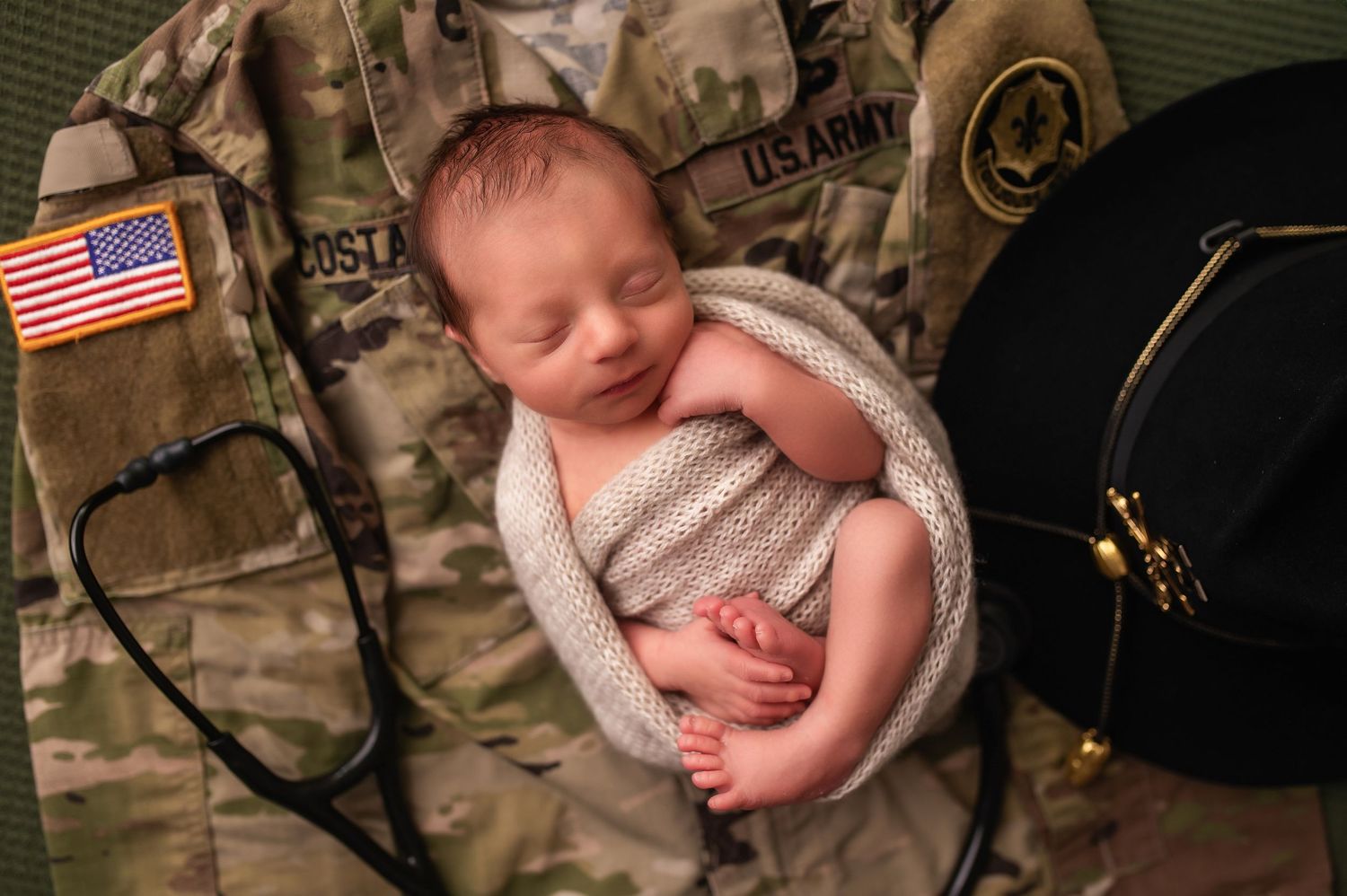 Military themed newborn photo with baby sleeping on camouflage uniform and American flag.
