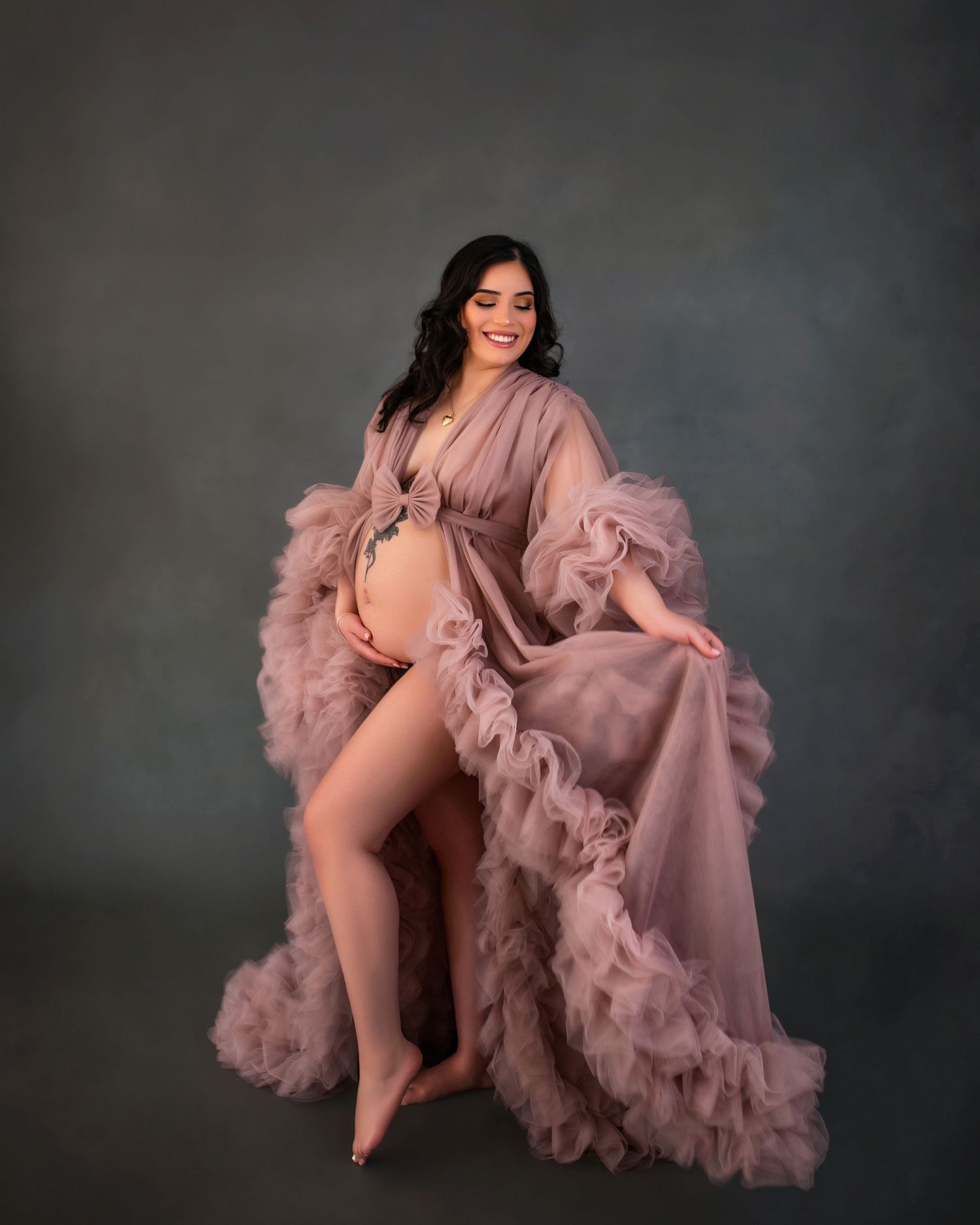 Pregnant woman in flowing dusty rose ruffle maternity gown posing gracefully in a professional studio photo shoot.