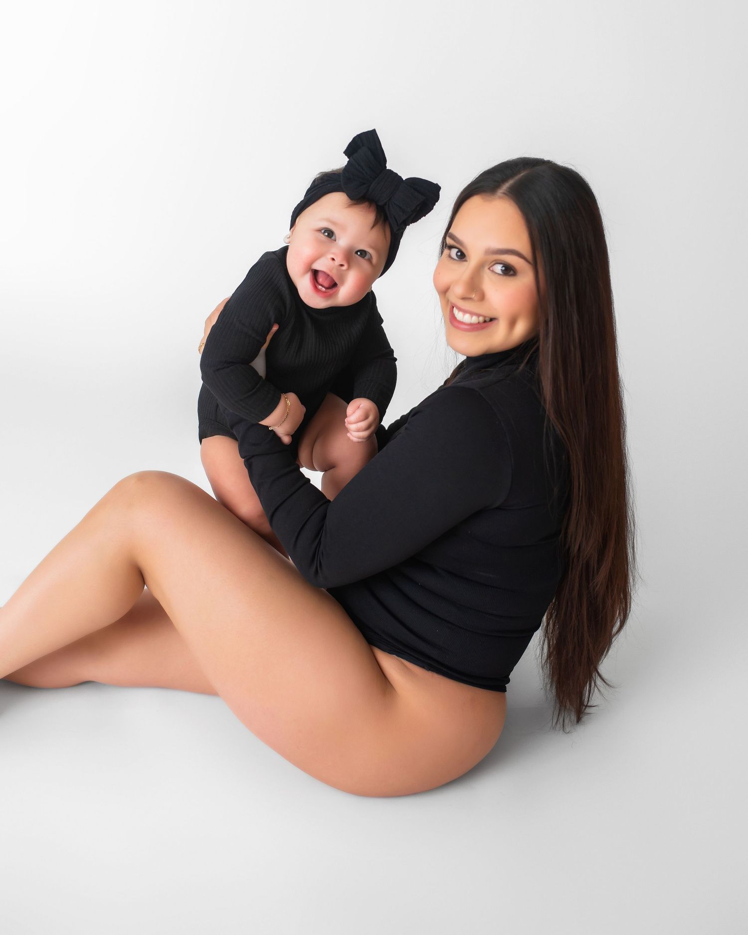 Mother and baby in matching black outfits during studio photoshoot on white background.