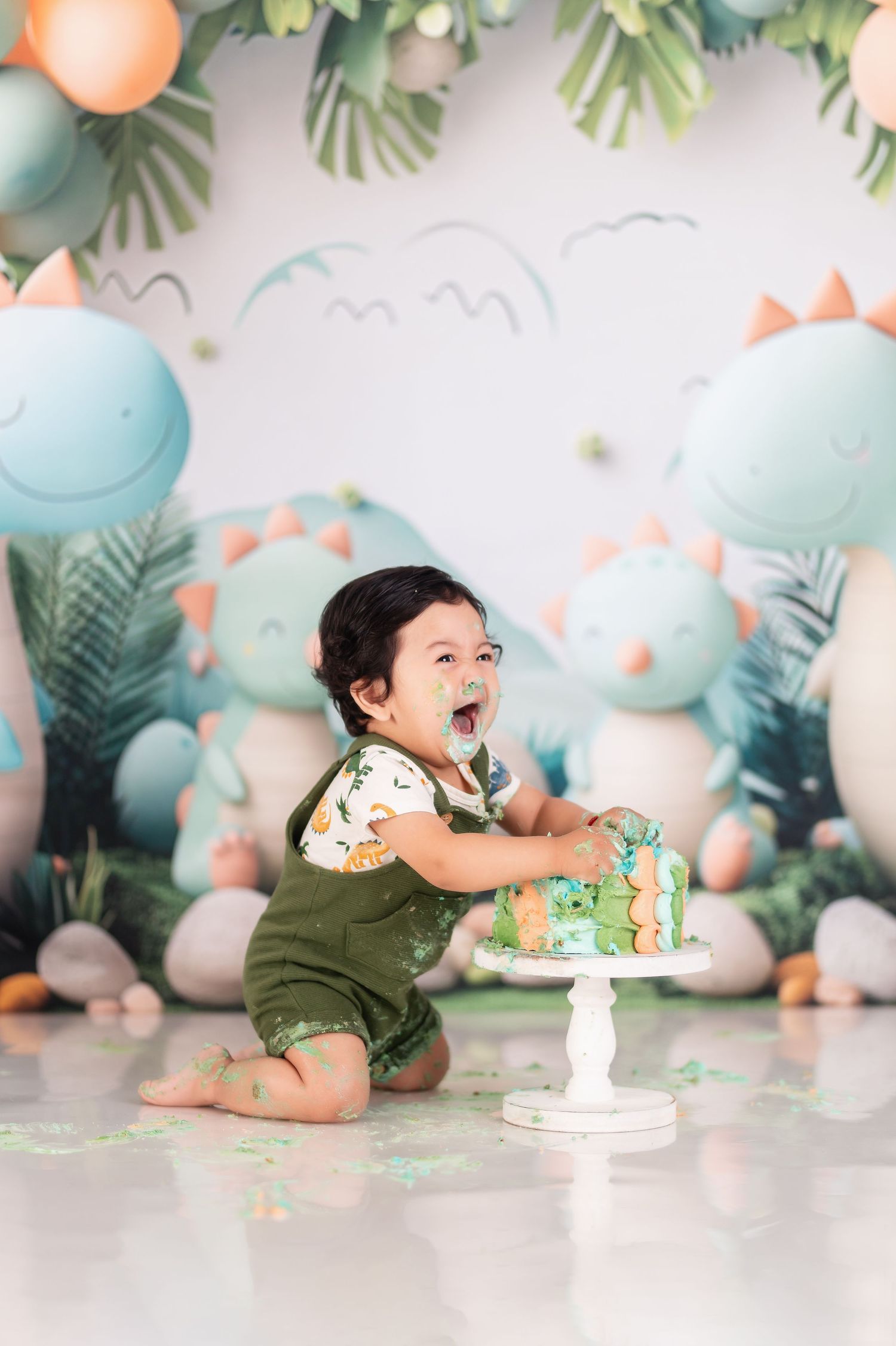 Cake smash photography session with pastel dinosaur themed backdrop and decorations.
