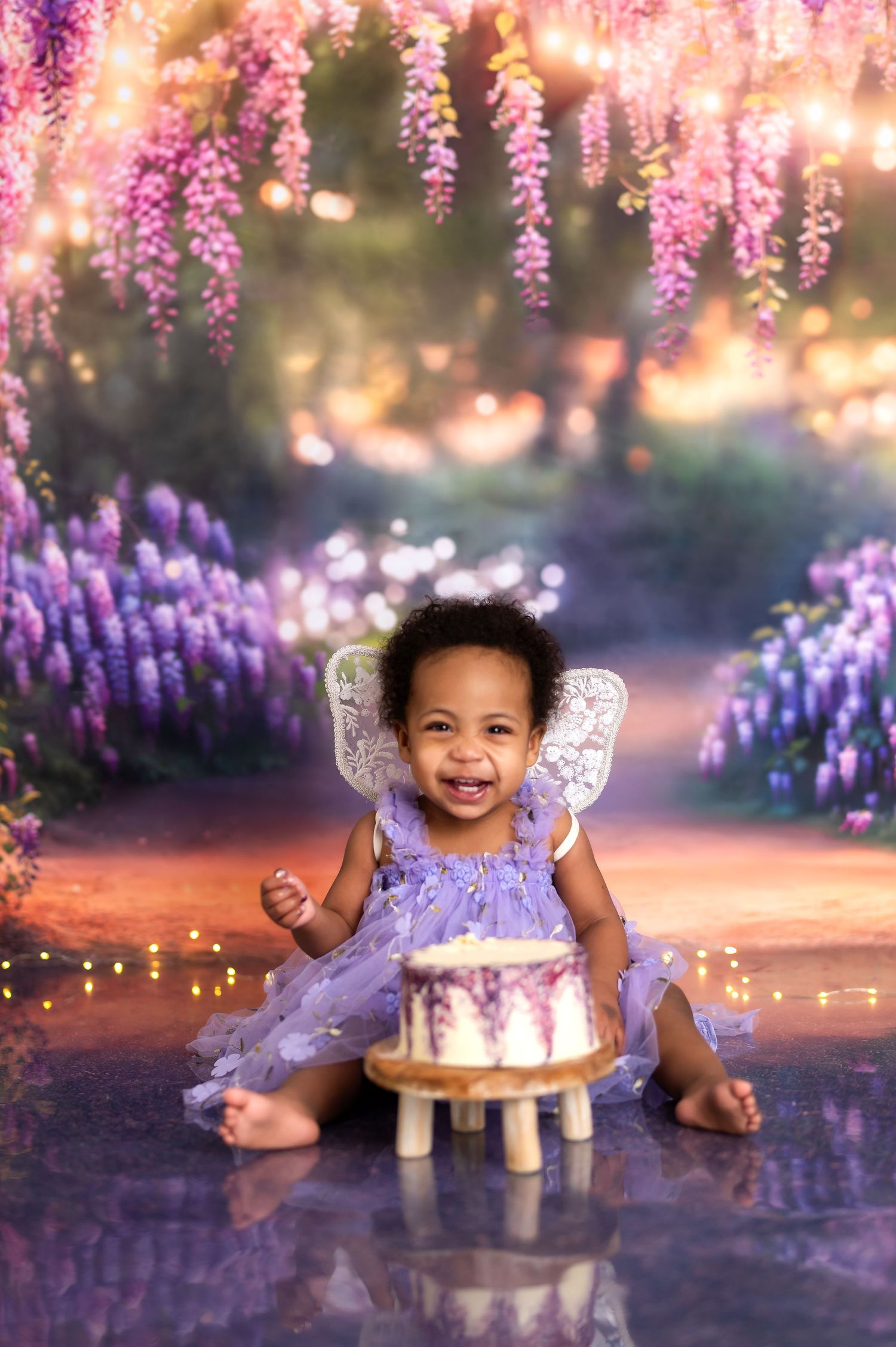 Enchanted garden cake smash setup with hanging wisteria flowers and twinkling lights.
