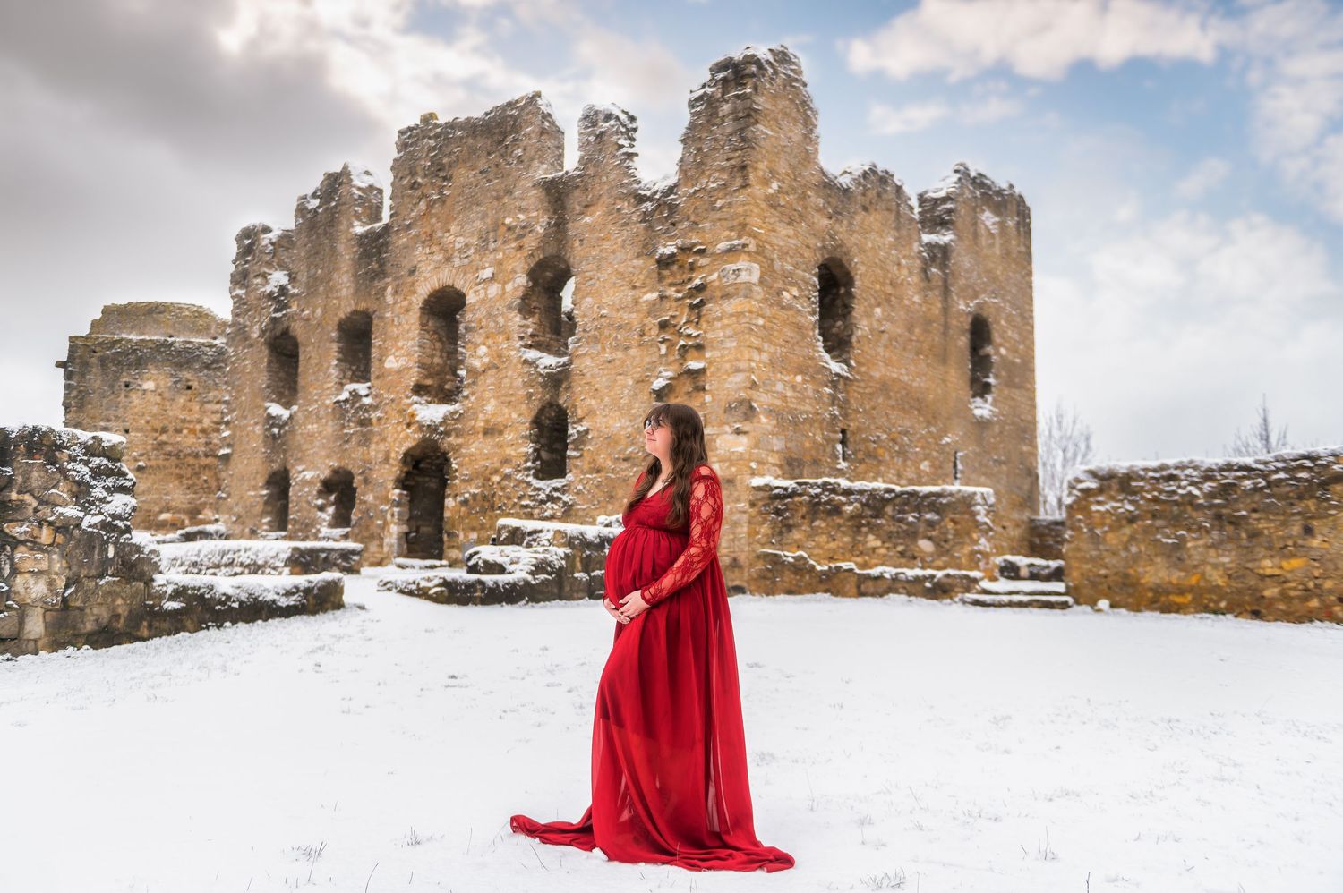 A red dress creates dramatic contrast against snow-covered castle ruins.