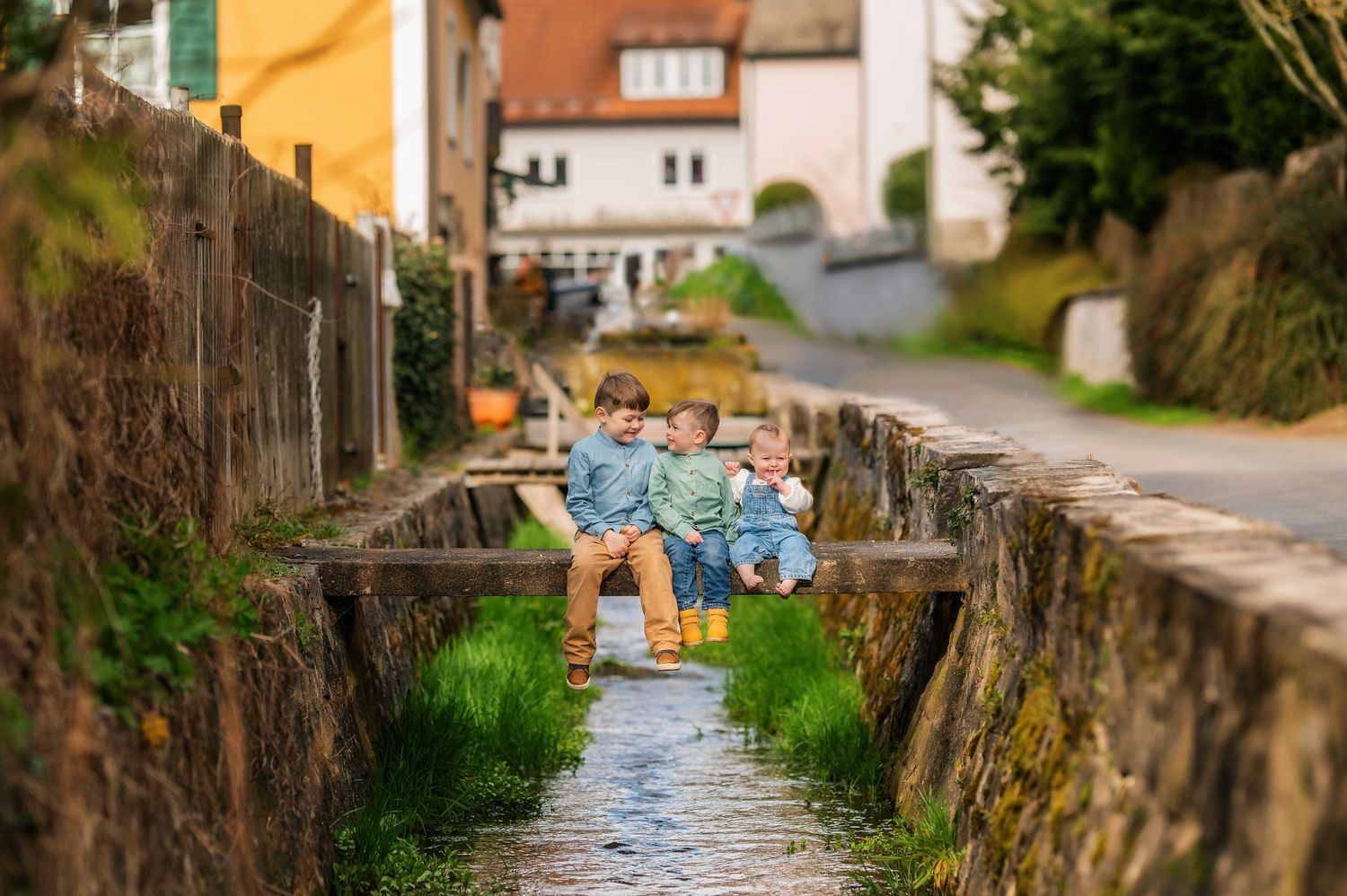 Yellow buildings line a rustic village street with stone walls and a small water channel.