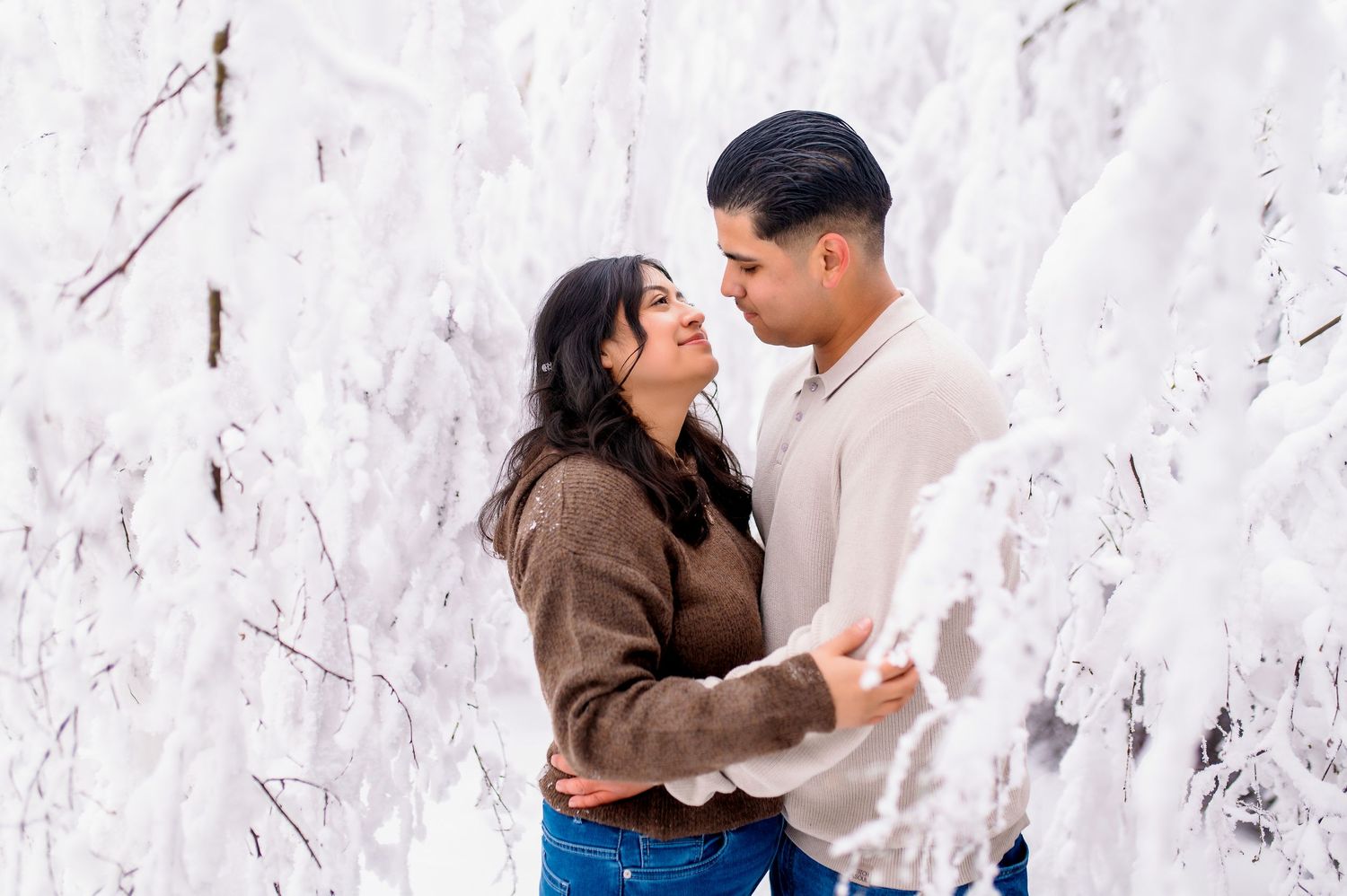 A romantic couple shares an intimate moment against a white textured wall, dressed in casual brown and beige outfits.