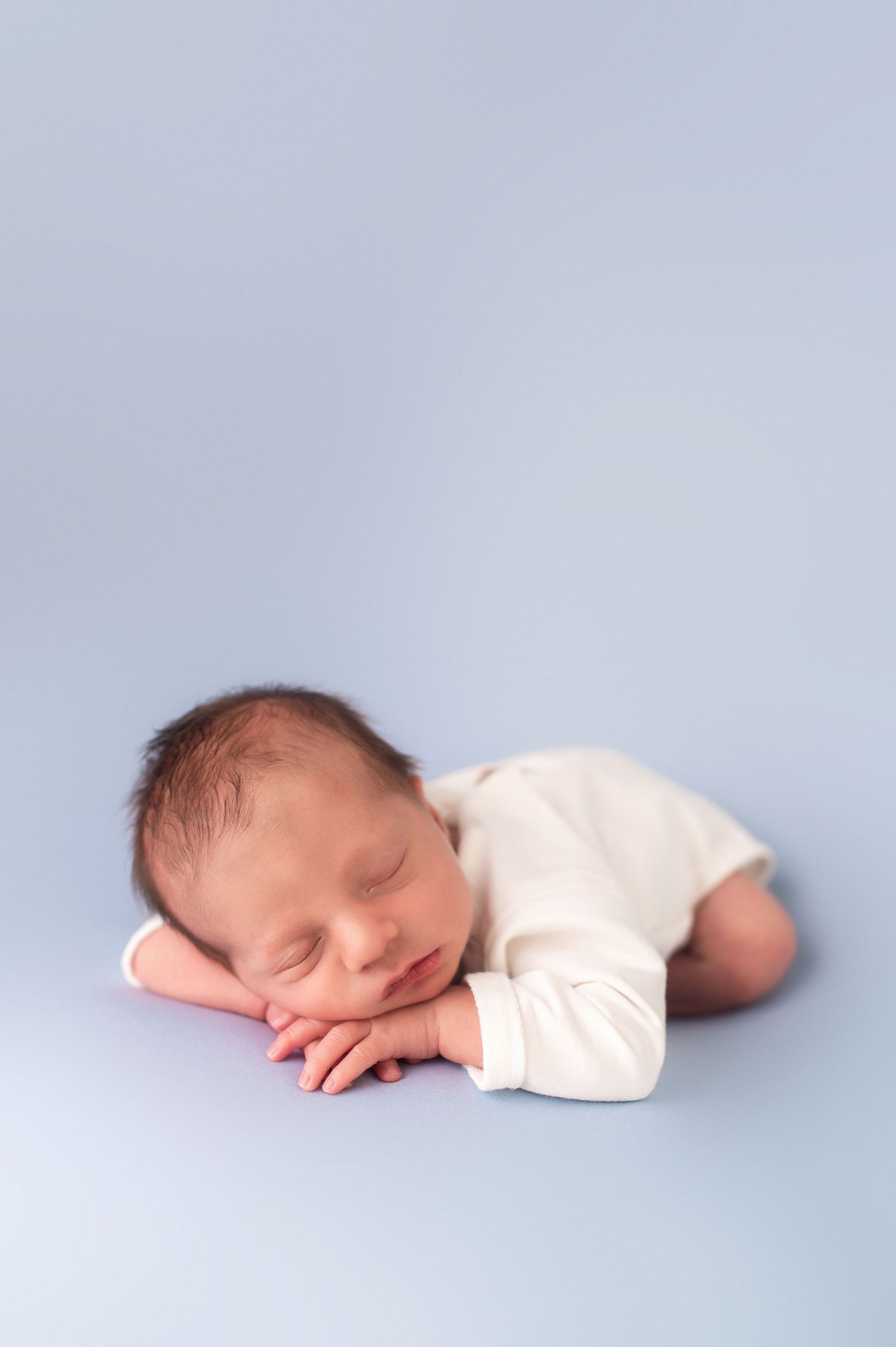Side view of sleeping newborn in white onesie on light blue background.