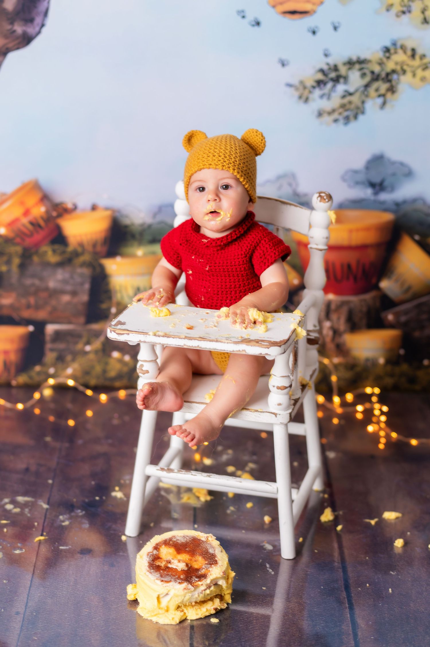 Fall themed cake smash session with baby in knit bear hat sitting in white chair.