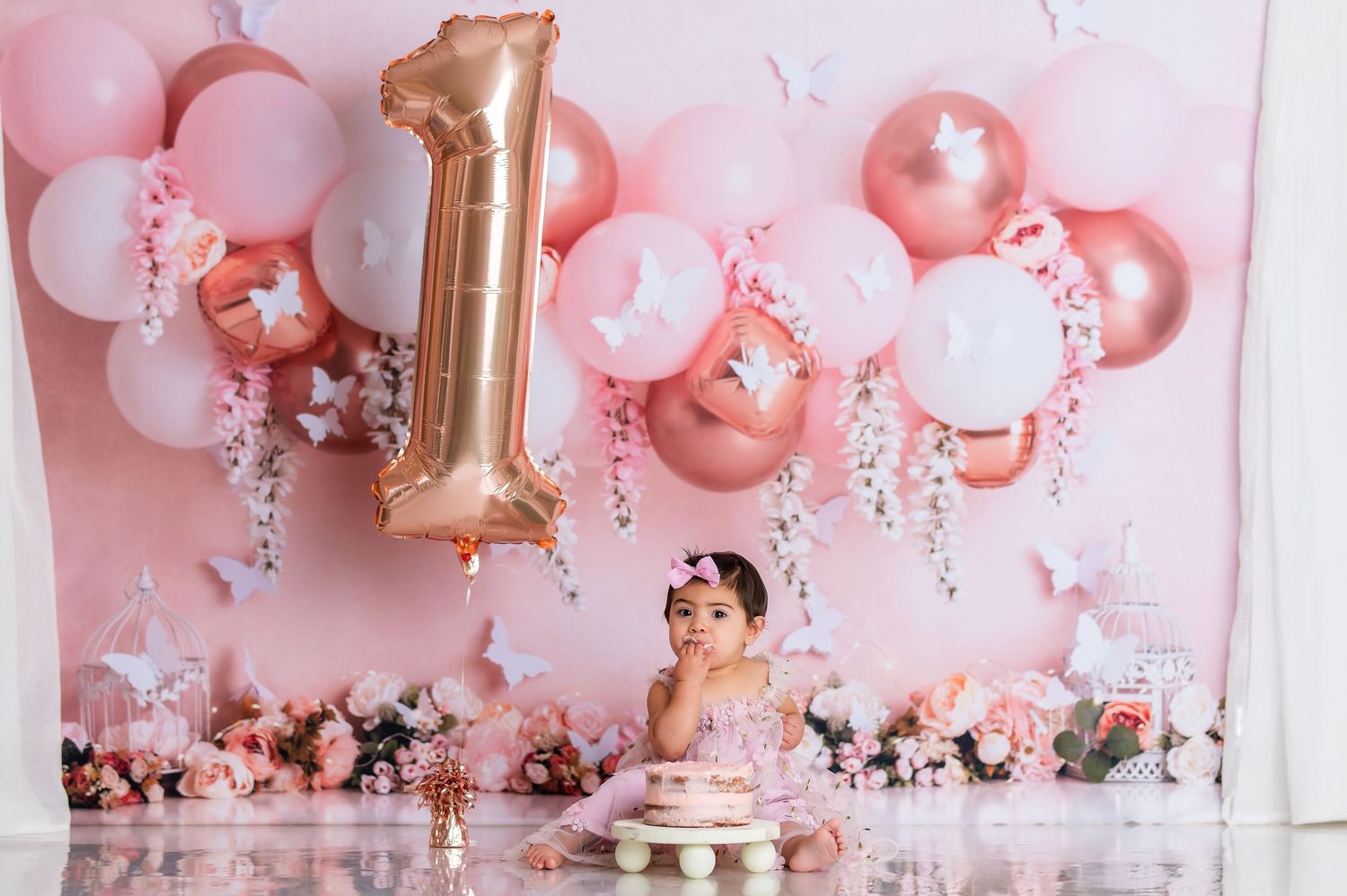 First birthday cake smash photo session with rose gold number one balloon and pink party decorations.