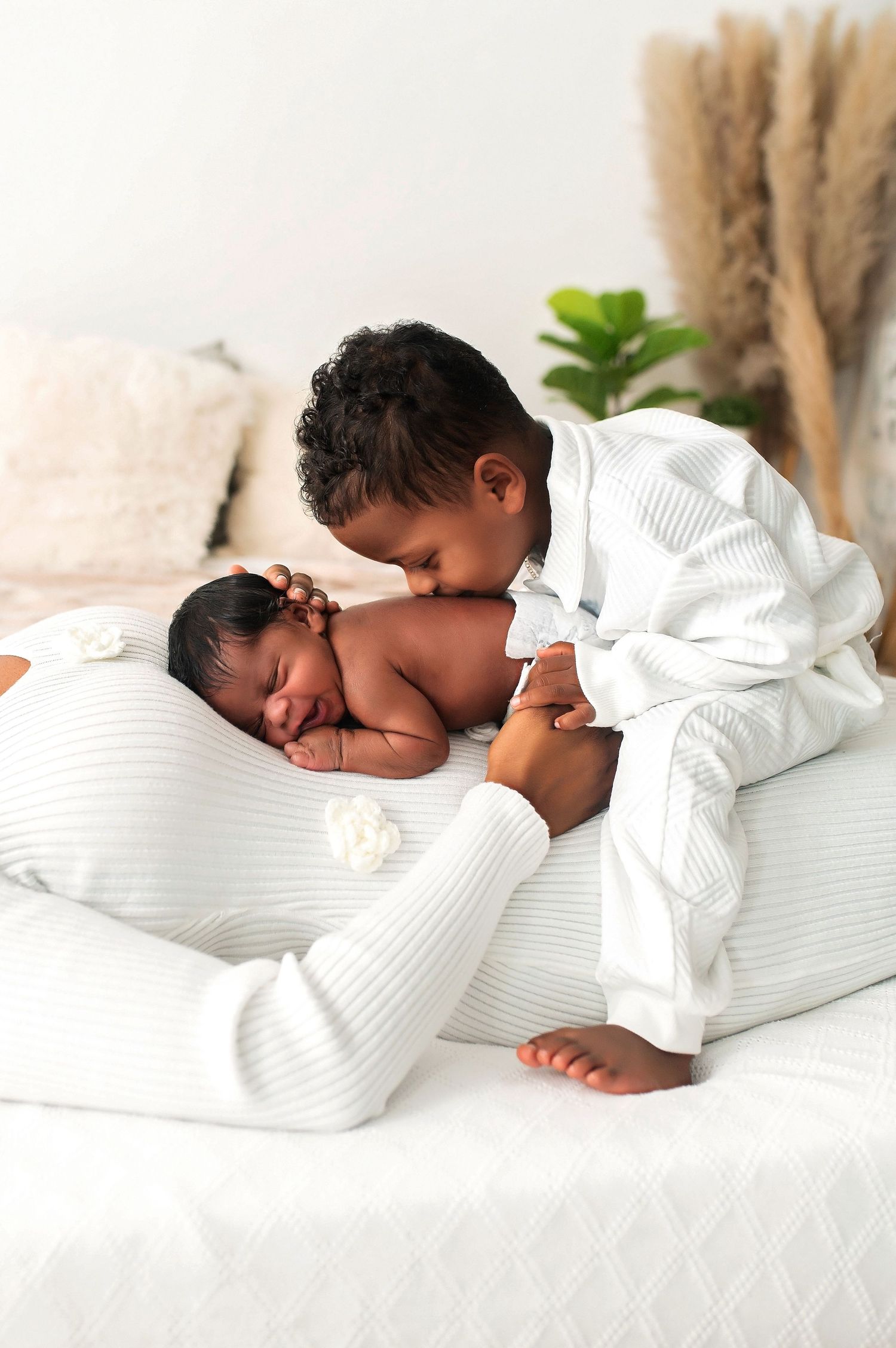 Sweet sibling moment with white-dressed children on soft white bedding.