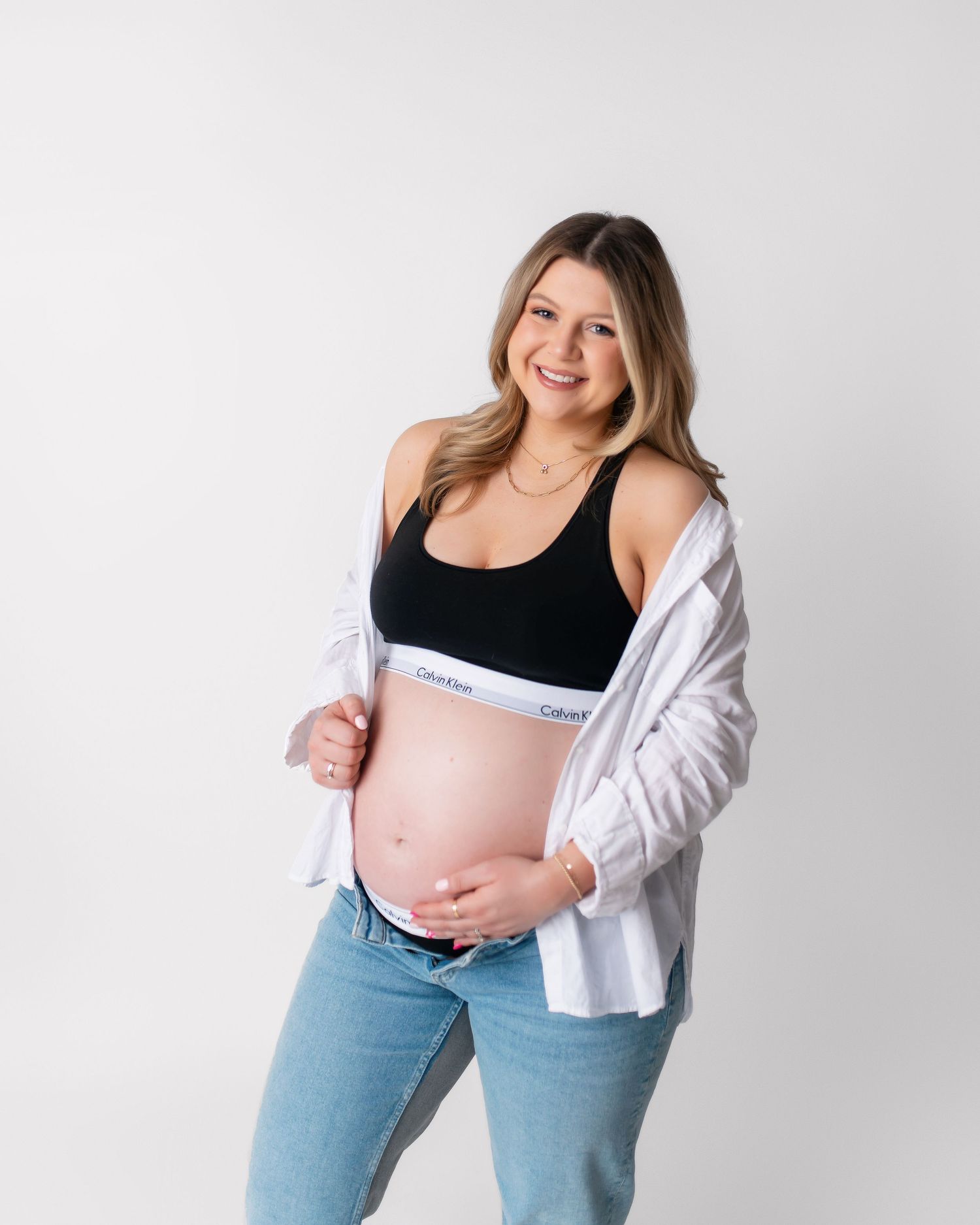 Expectant mother in layered black and white tops shows baby bump while smiling at camera.