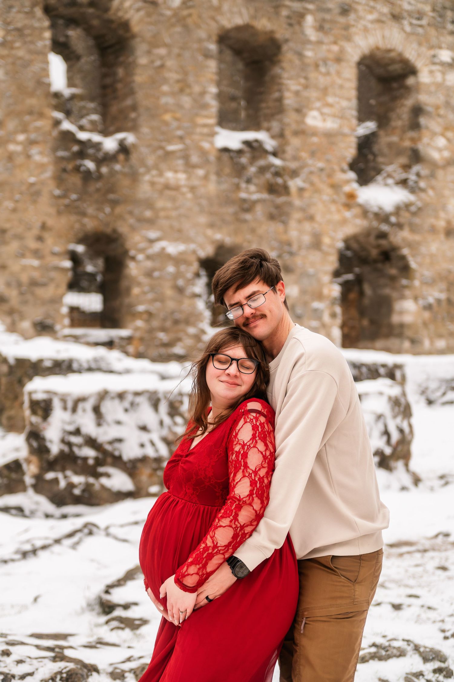Couple embracing near snow-dusted medieval castle ruins during winter photoshoot.