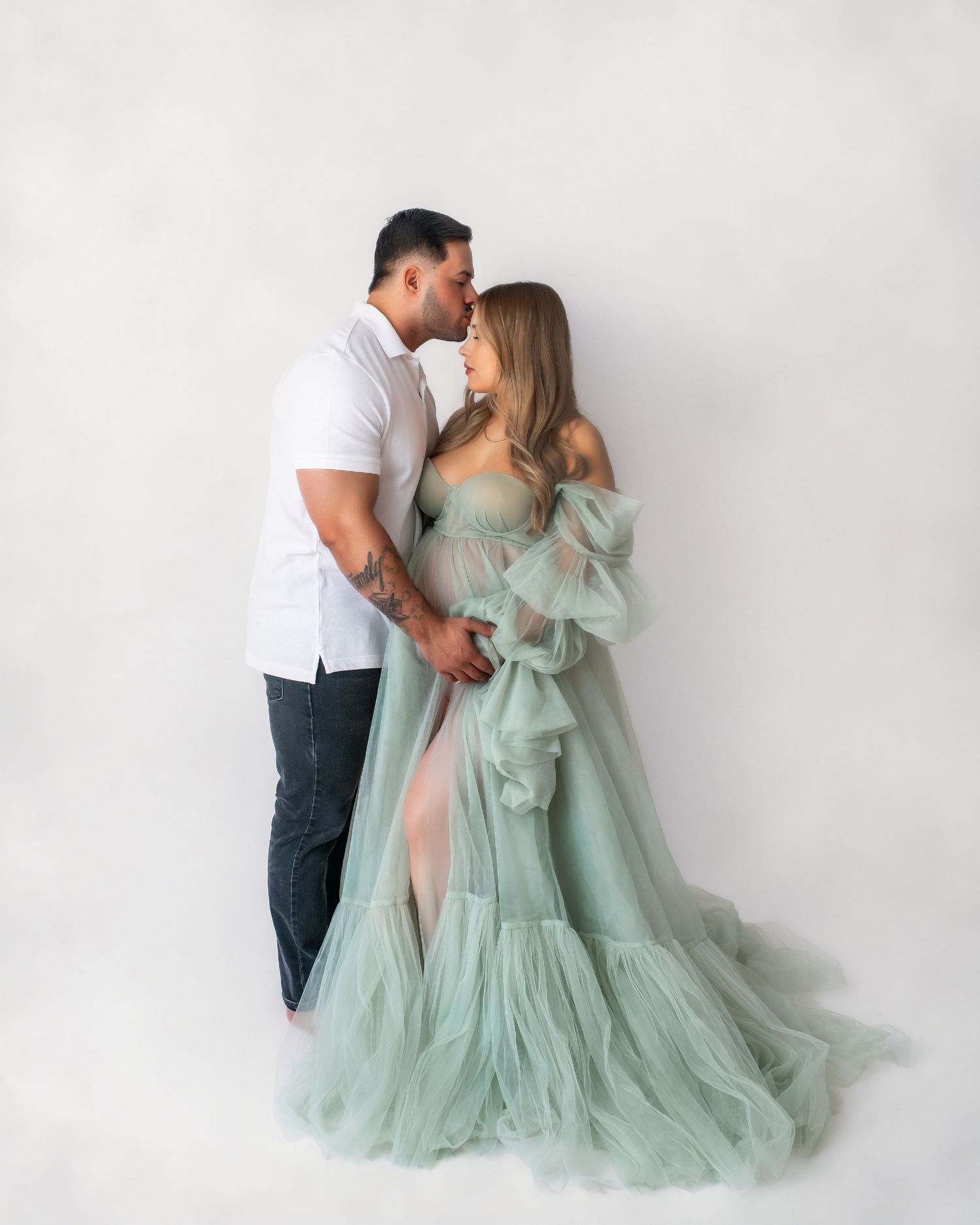 Couple in romantic maternity pose wearing white and mint green formal attire.