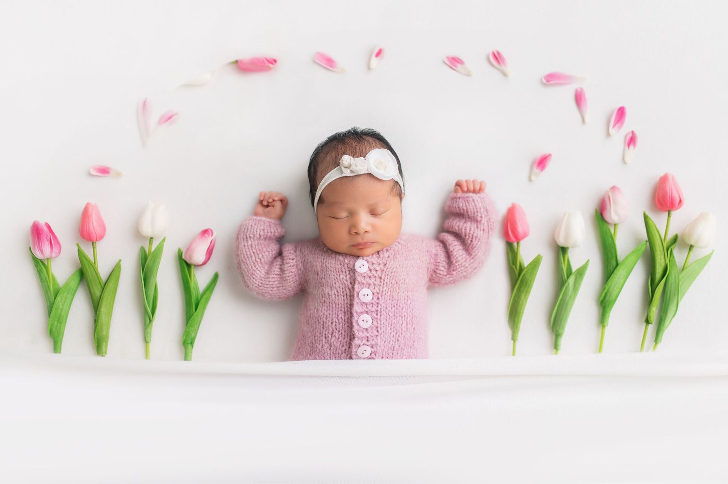 Sweet newborn photography setup with pink tulips and soft white background.