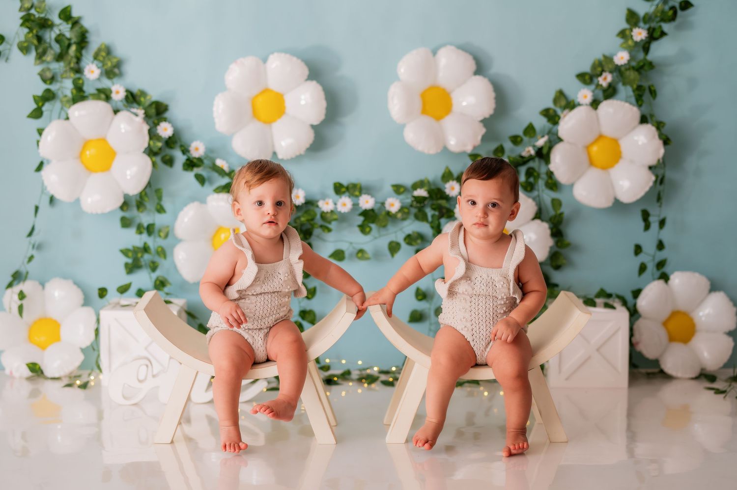 Baby photoshoot setup with daisy flowers and vines against blue backdrop.