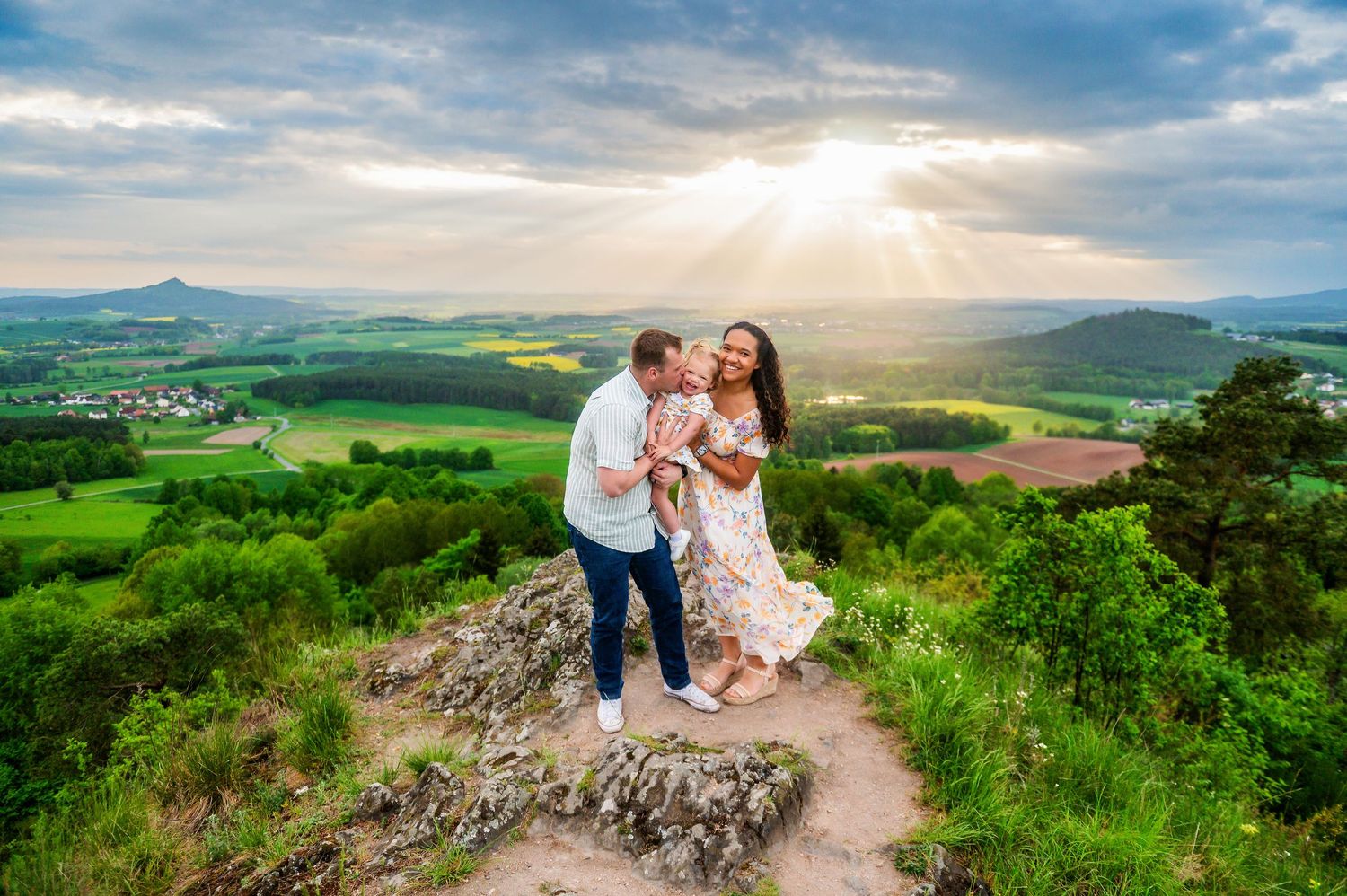 Couple sharing romantic moments on a scenic mountain overlook with rolling green hills and dramatic sky at sunset.
