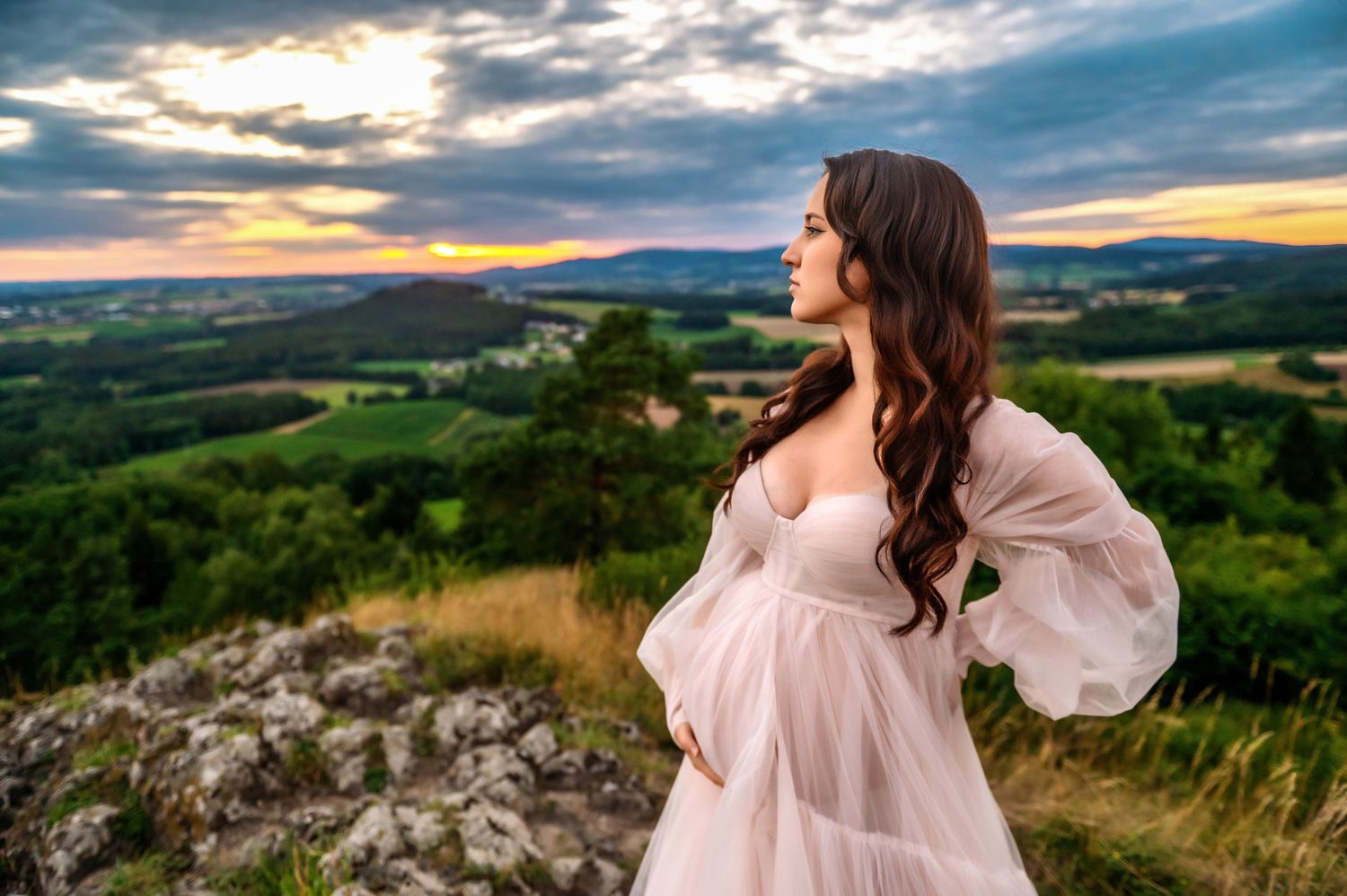 A person in a flowing pink dress twirls on a hilltop during golden hour with scenic countryside views in the background.