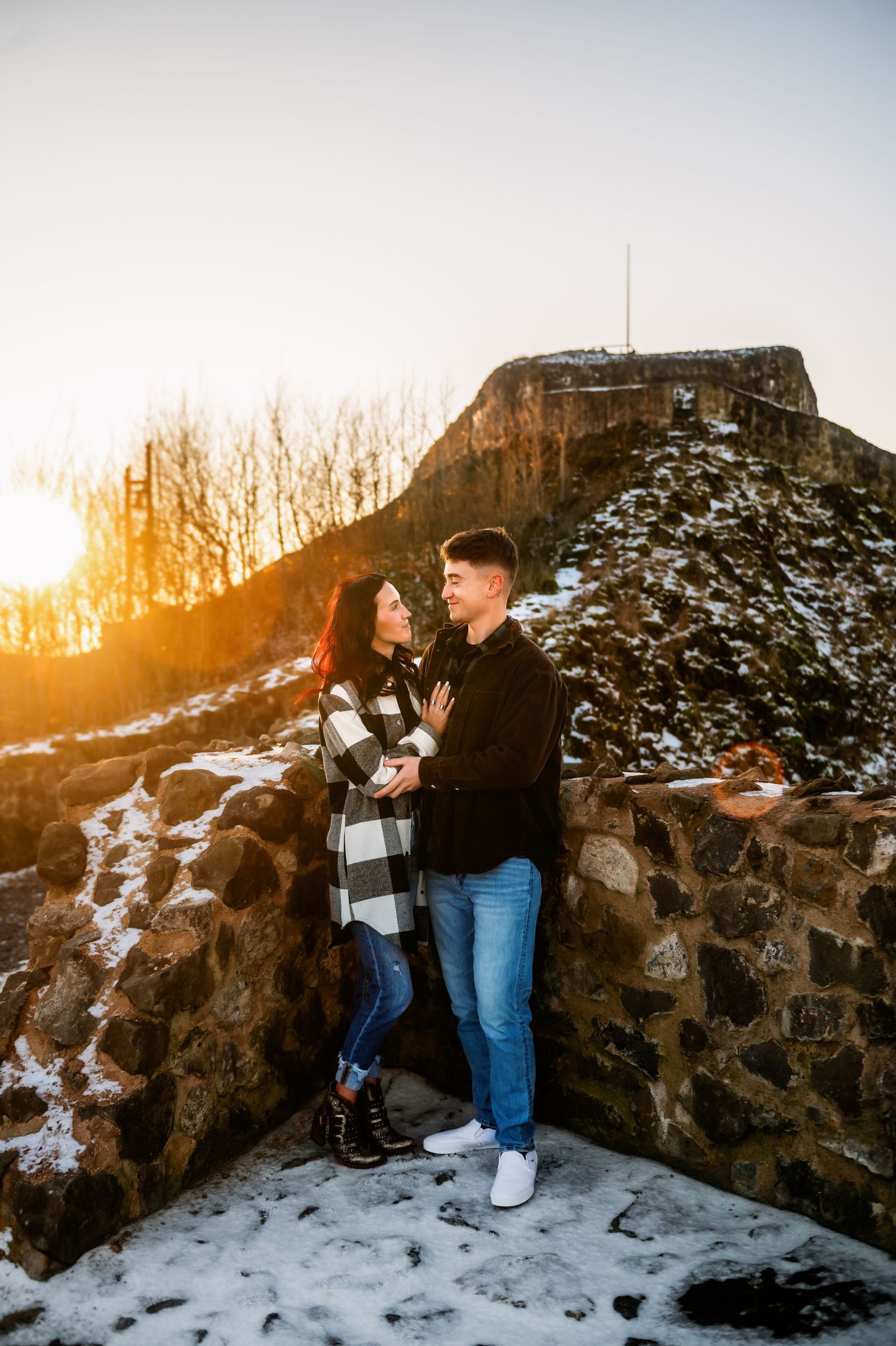 A couple shares an intimate moment at sunset on a snow-dusted stone wall.